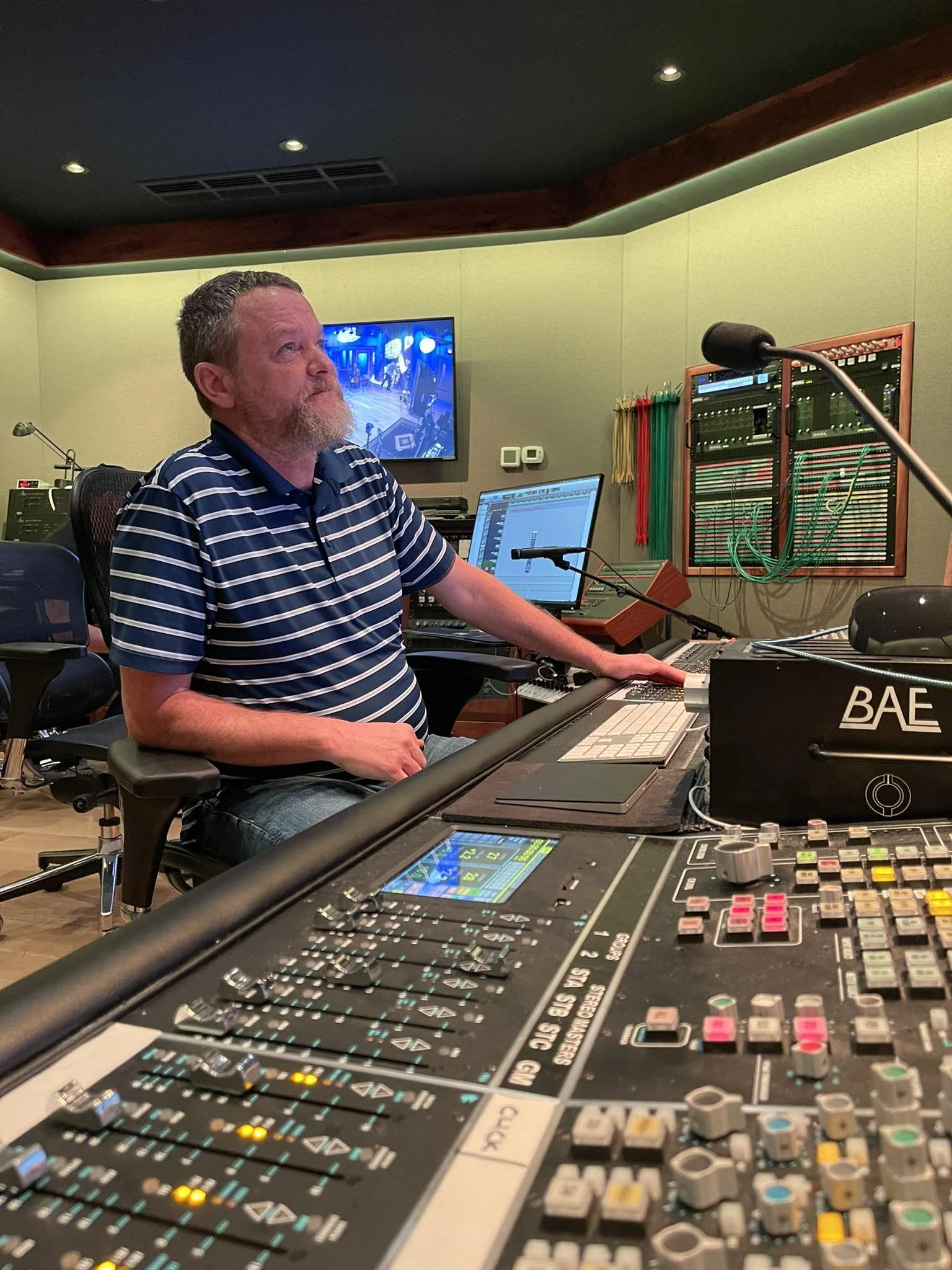 A sound engineer sitting at a mixing console in a recording studio, with music production equipment, computers, and monitors.