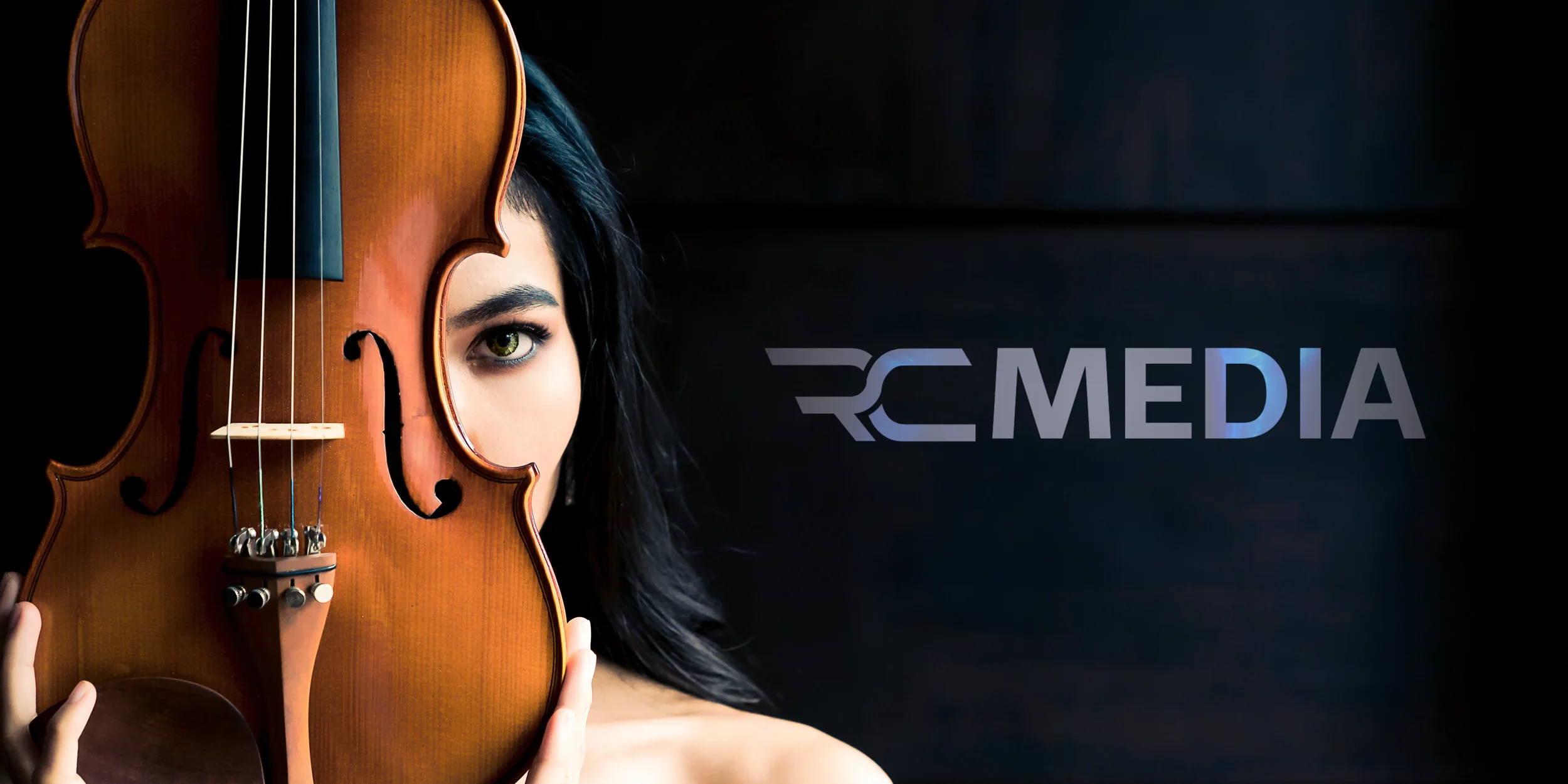 A woman with dark hair and green eyes holding a violin up to her face, covering half of her face, on a dark background with the text 'RC MEDIA' on the right side.