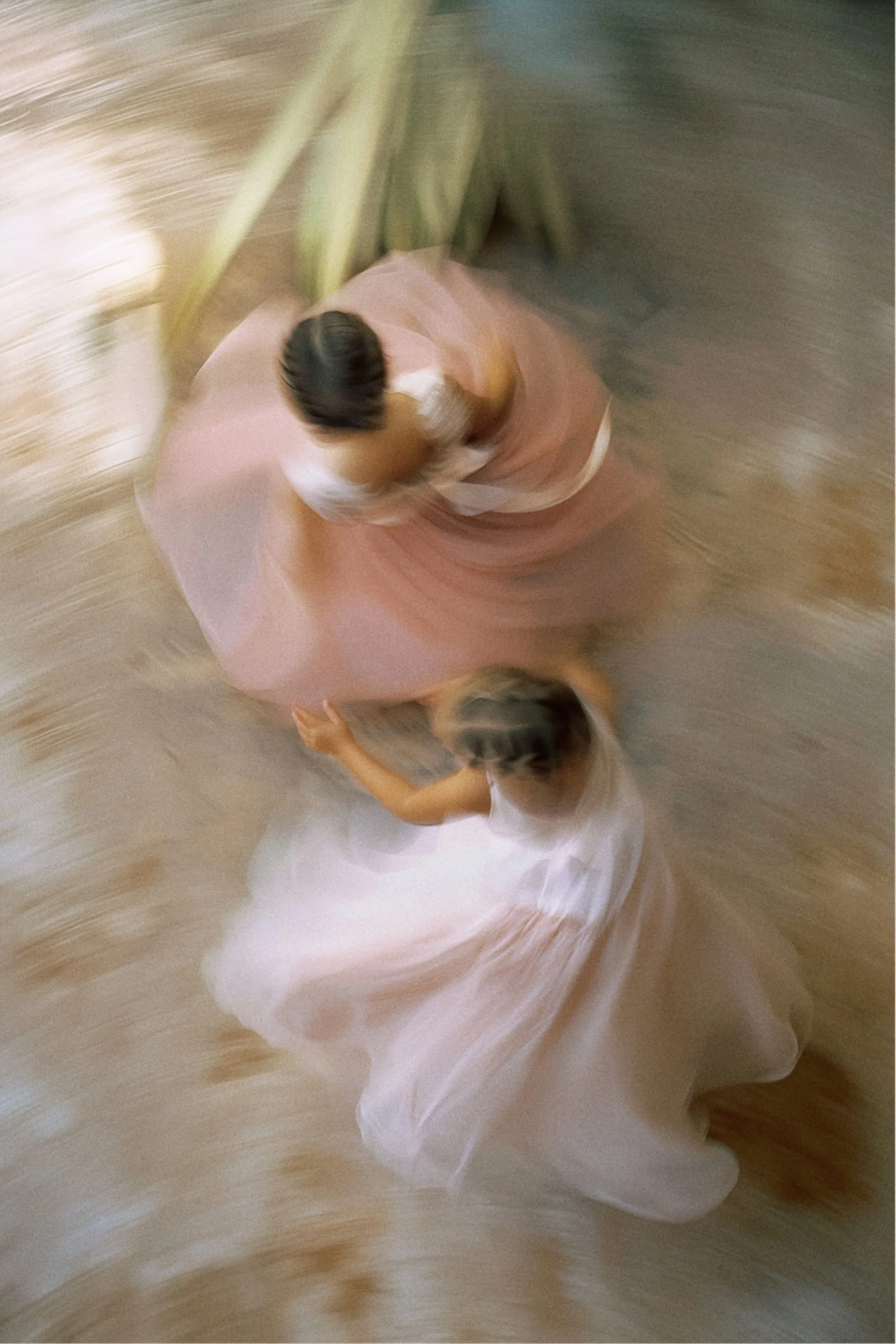 A top-down view of a woman spinning in a pink dress with a young girl in a light-colored dress, with both appearing to dance or twirl.