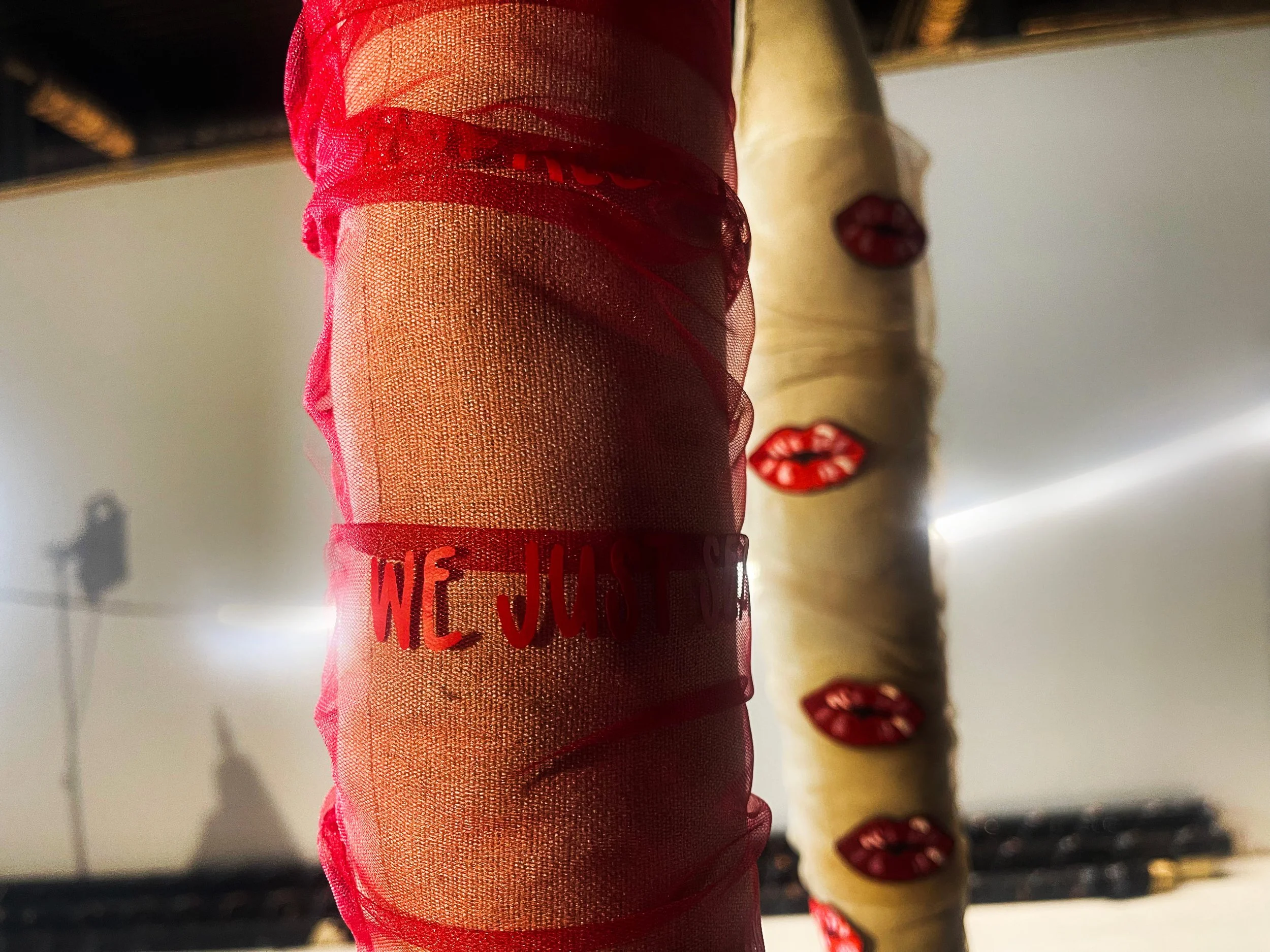 A close-up view of a decorated cake with red mesh and lips patterns, with another cake in the background topped with red lips decorations, photographed from below.