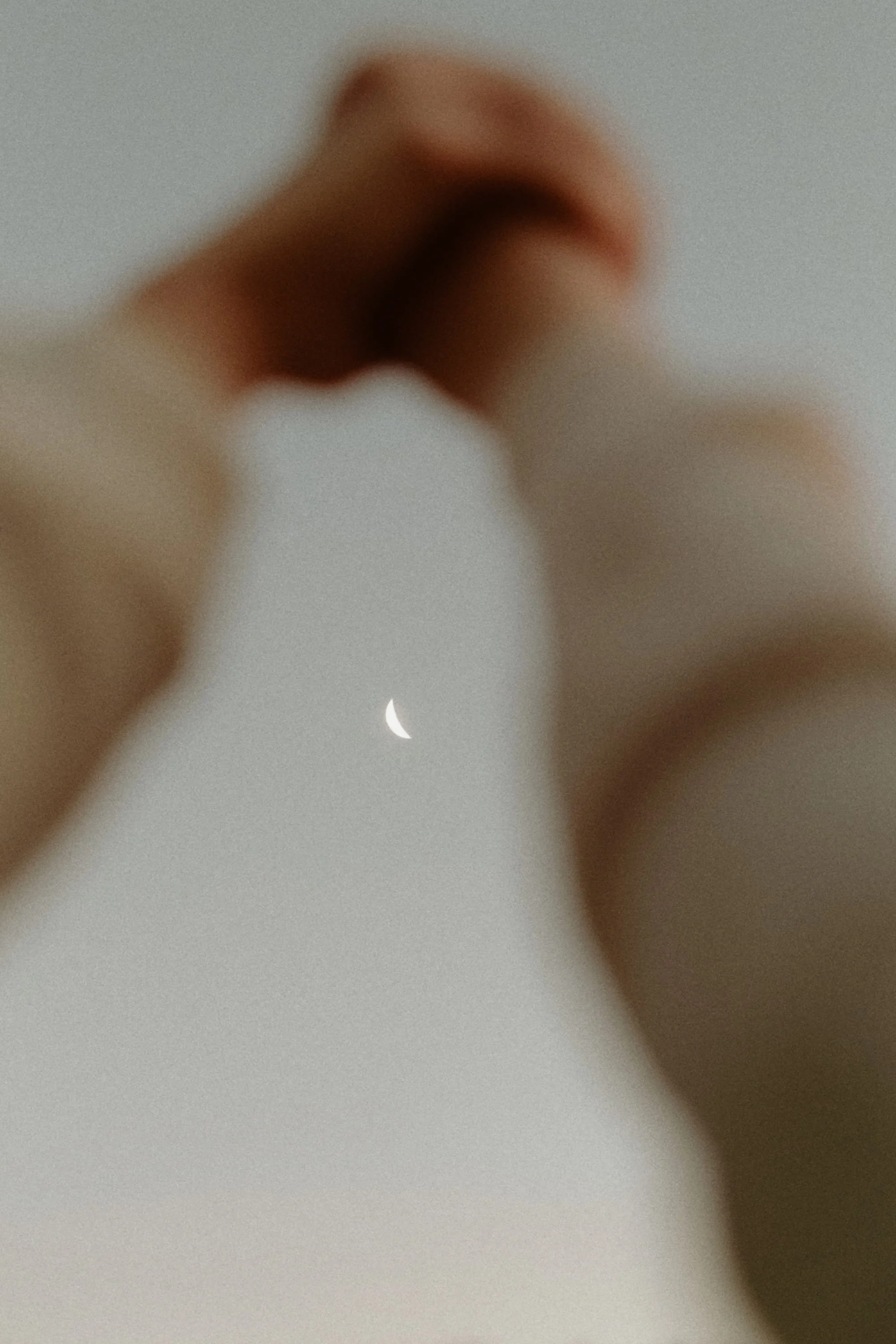 Close-up of two fingers pinching a crescent moon in the sky, with a blurred background.