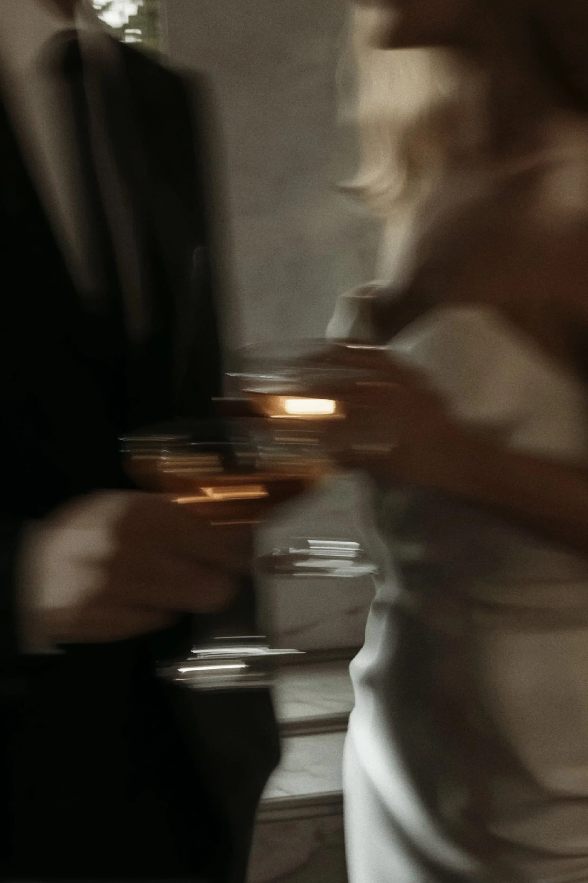 A person wearing a white shirt holding a glass of drink in a dimly lit setting.
