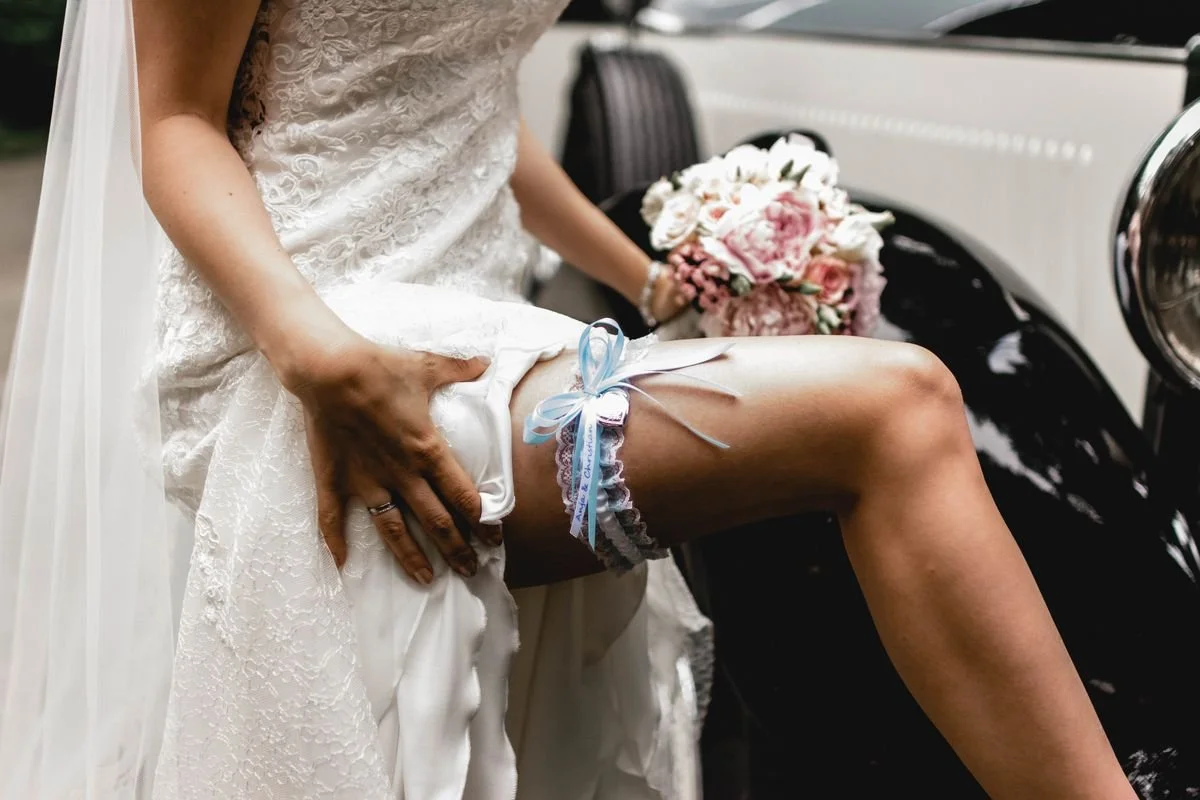 Bridesmaid lifting her dress to show her garter at a wedding, with a bouquet of flowers in the background.