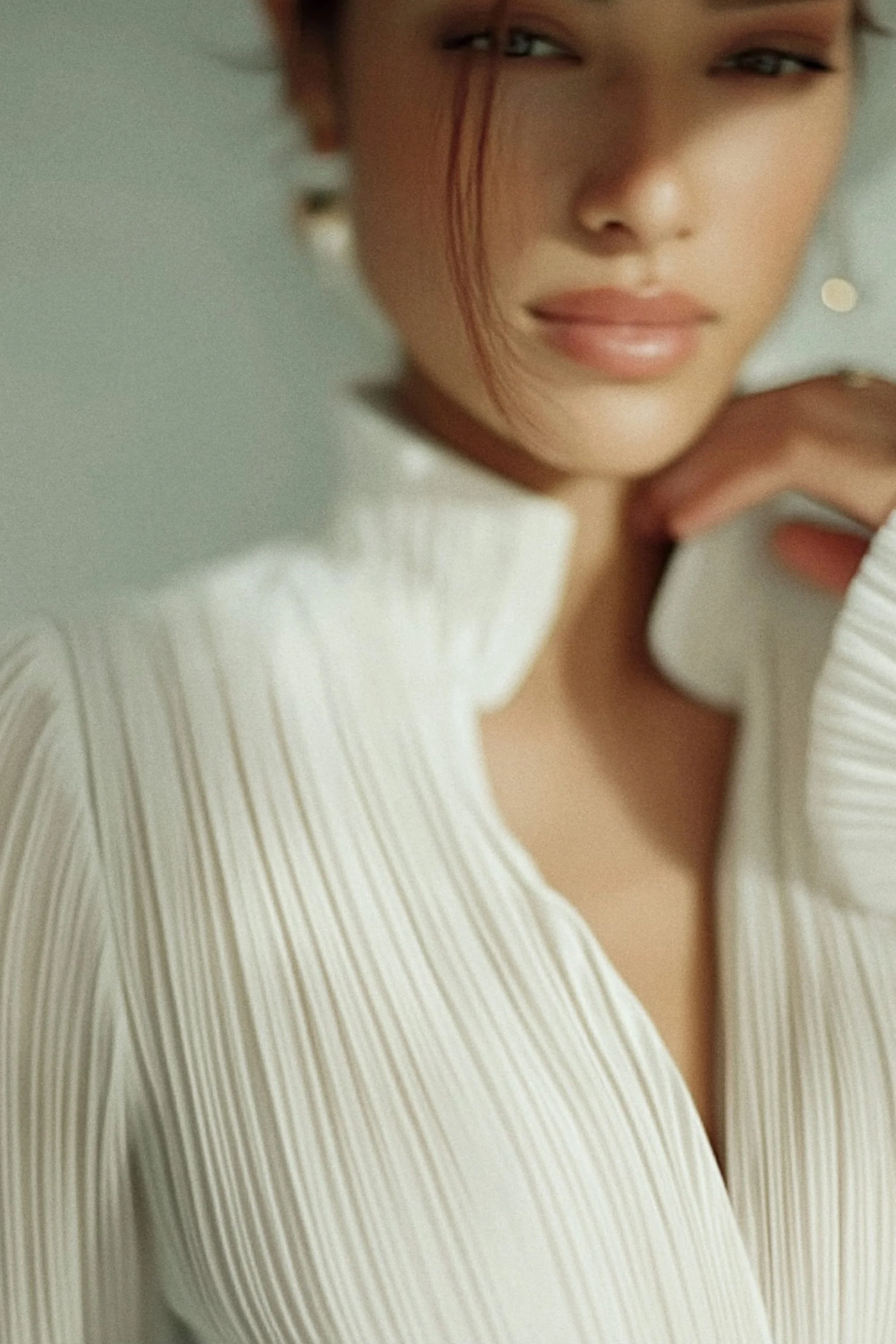 Close-up of a woman with fair skin, dark hair, and subtle makeup wearing a white, ribbed, high-neck sweater, with a soft expression.
