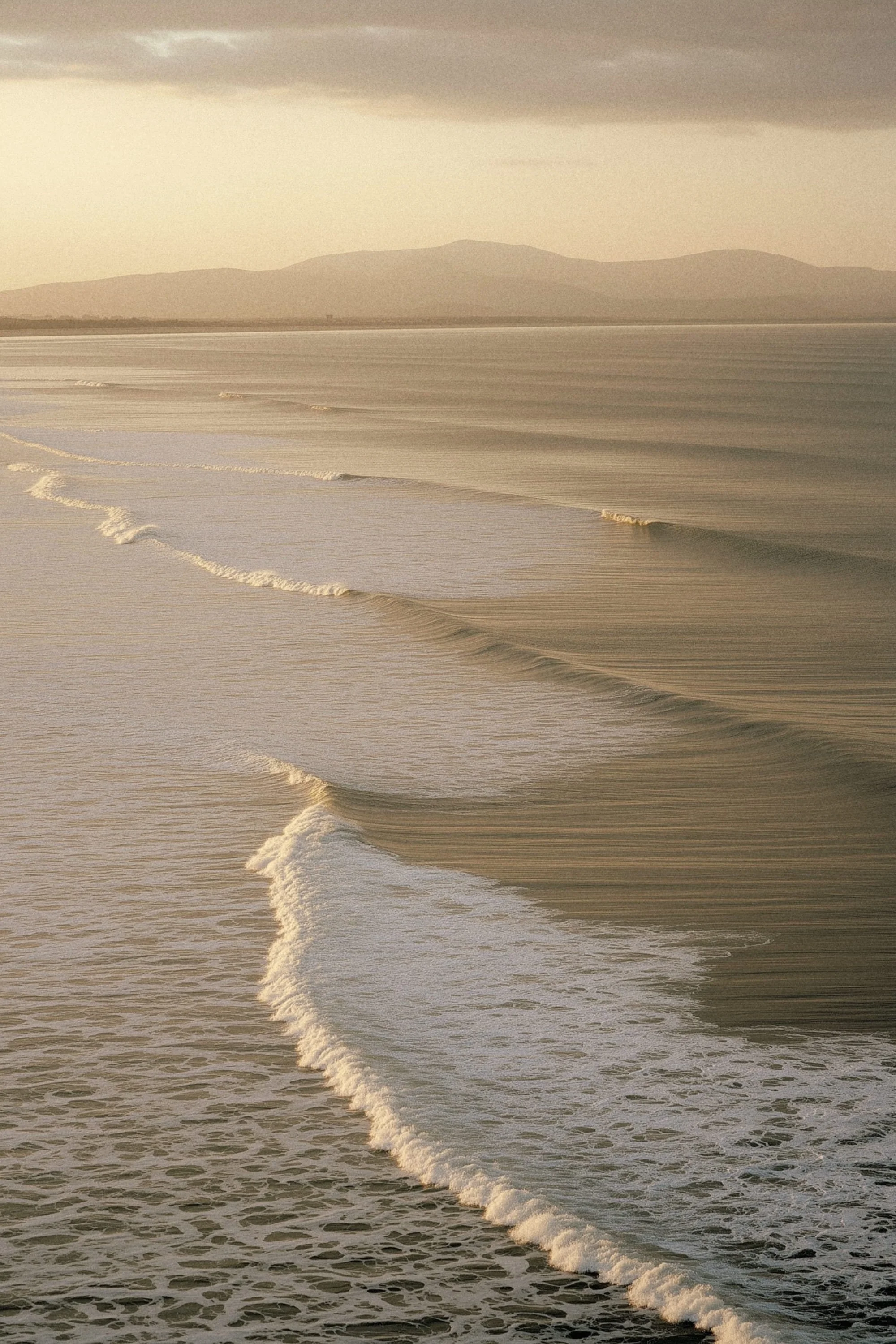 Calm ocean with gentle waves and distant mountains under a cloudy sky.