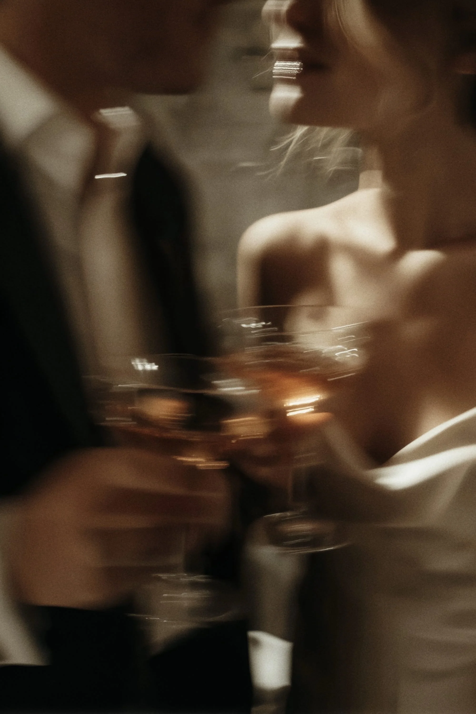 A close-up of a couple kissing while holding glasses of champagne or wine, possibly at a romantic or celebratory event.