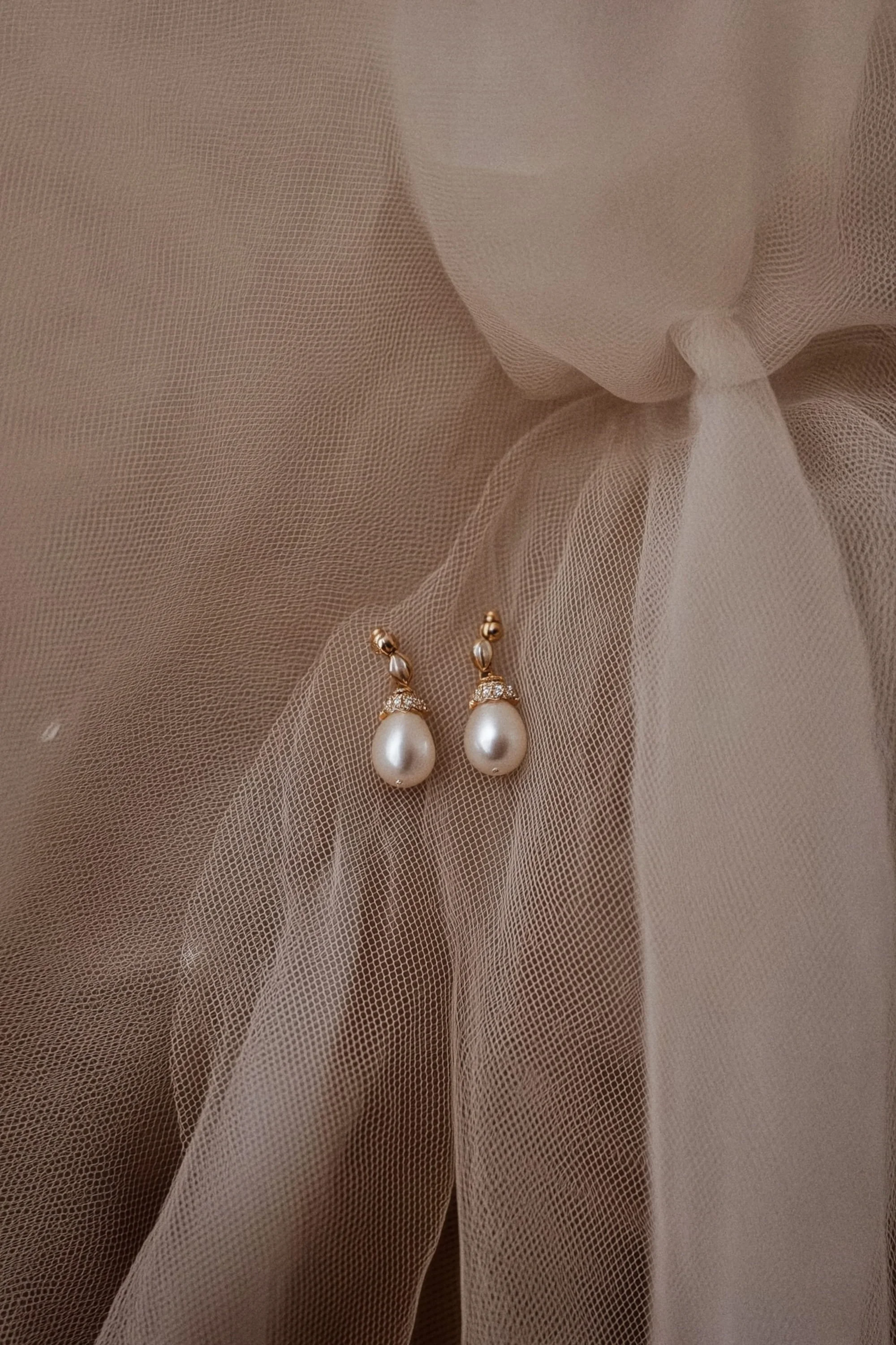 Pearl earrings with diamond accents resting on beige fabric with a tulle overlay.