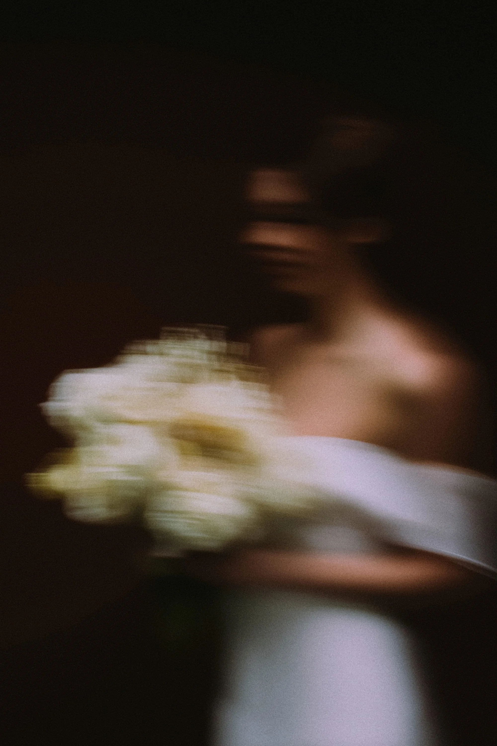 Blurred image of a person holding a bouquet of flowers in a dark setting.