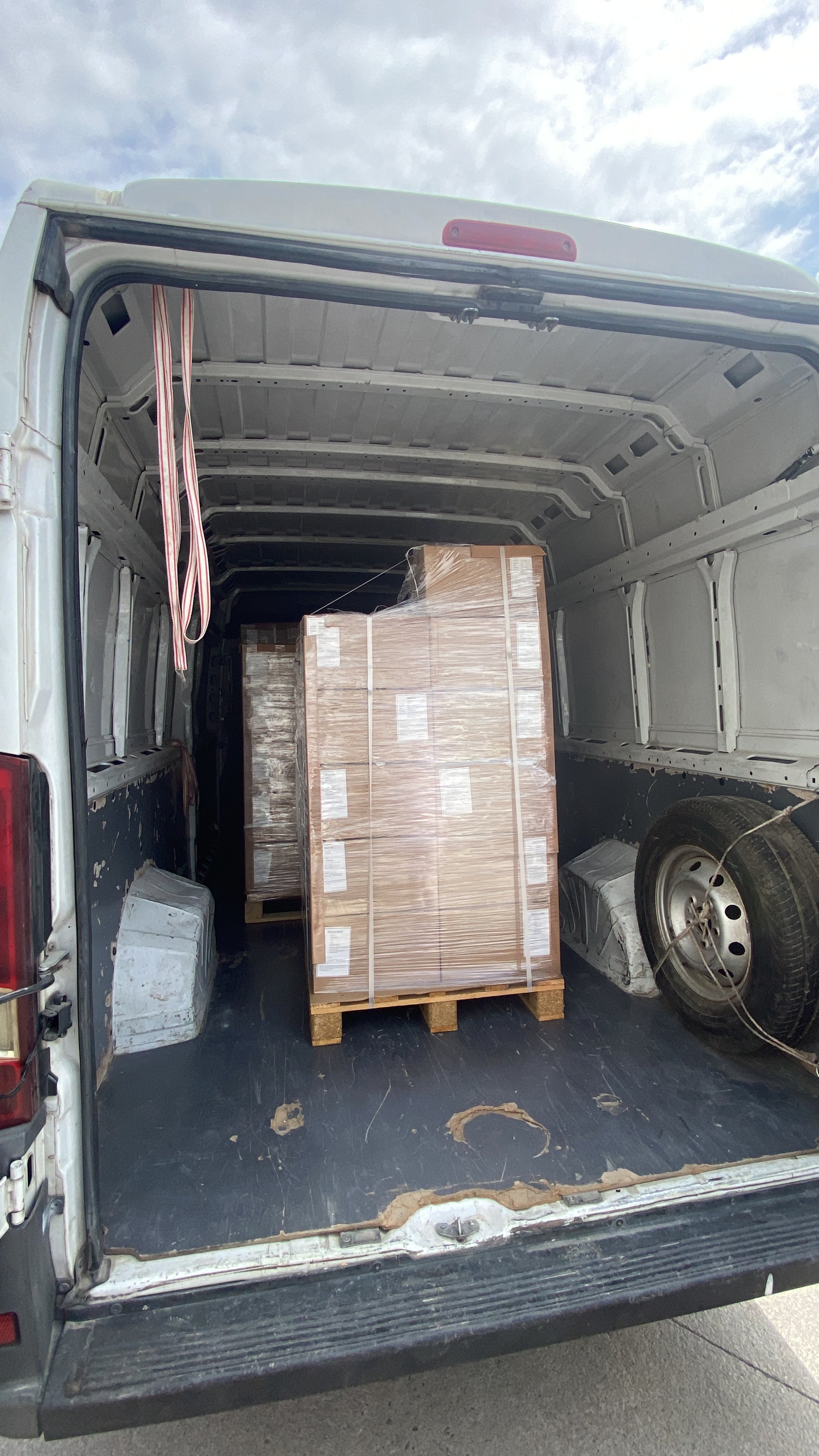 Inside the back of a cargo van with large pallets of boxed goods secured with plastic wrap.
