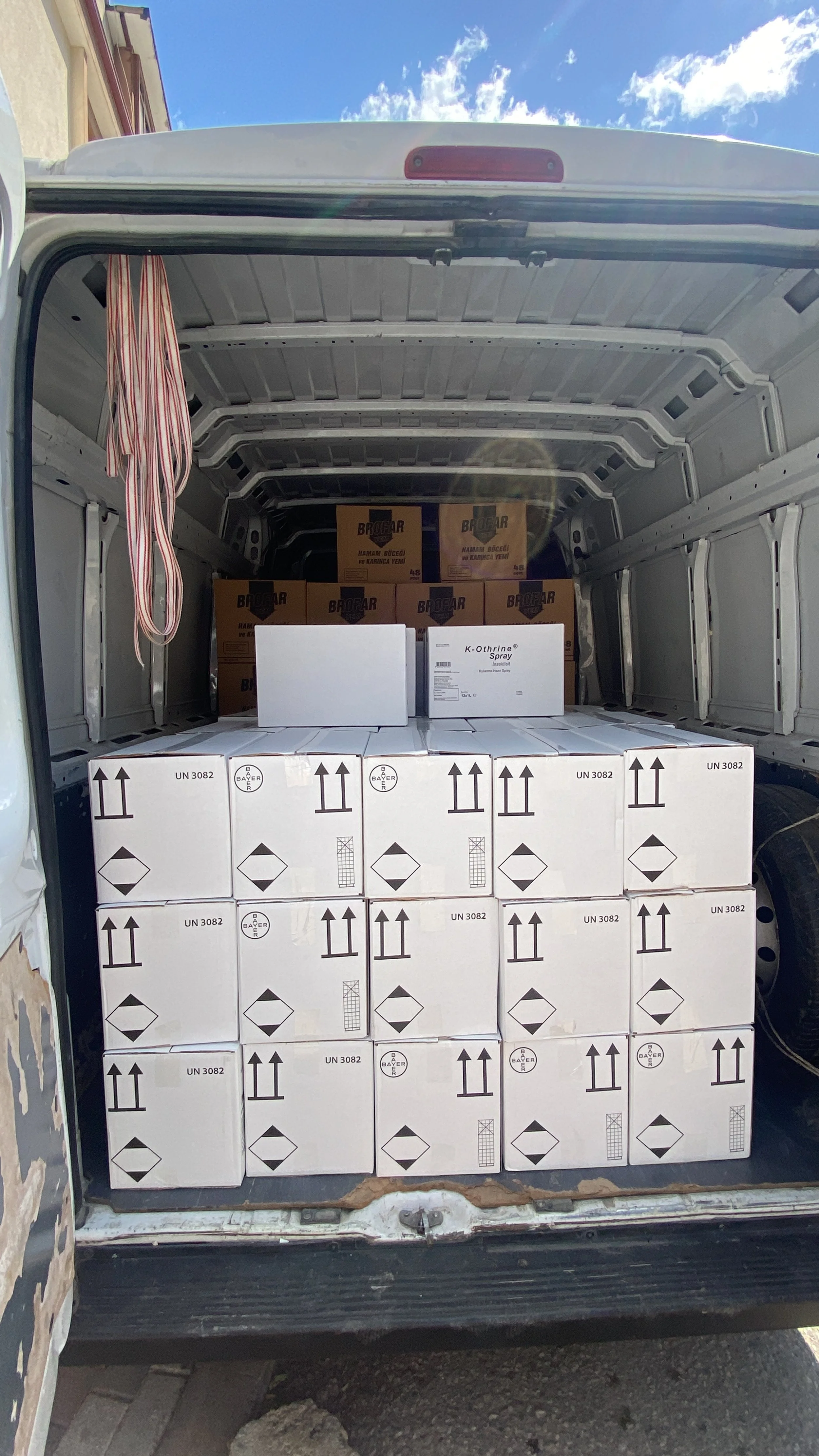 The back of a delivery van filled with stacked white boxes marked with hazard symbols and arrows, and some brown boxes in the interior.