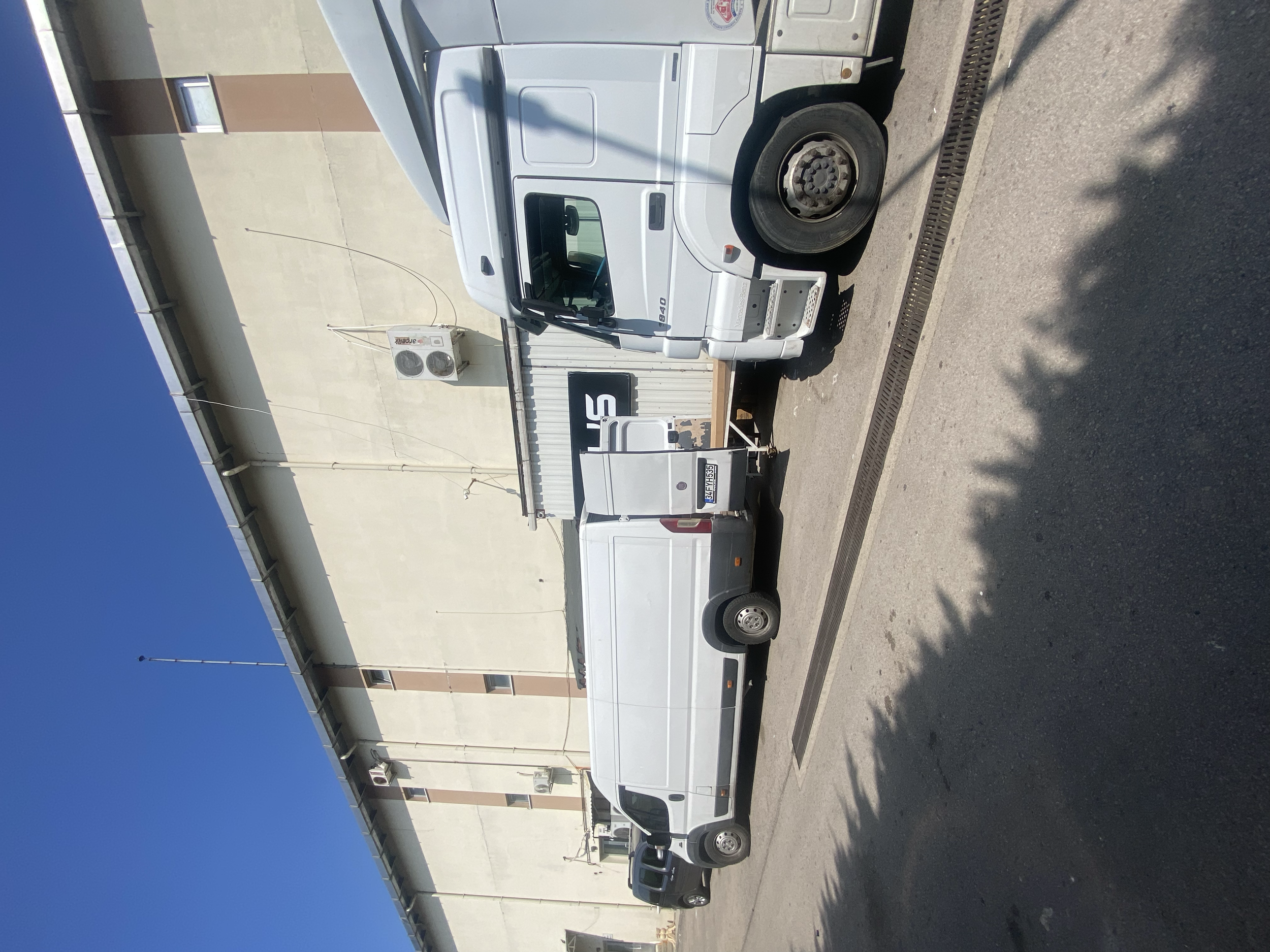 A white utility van parked next to a beige building with air conditioning units and a sign that reads 'S'.