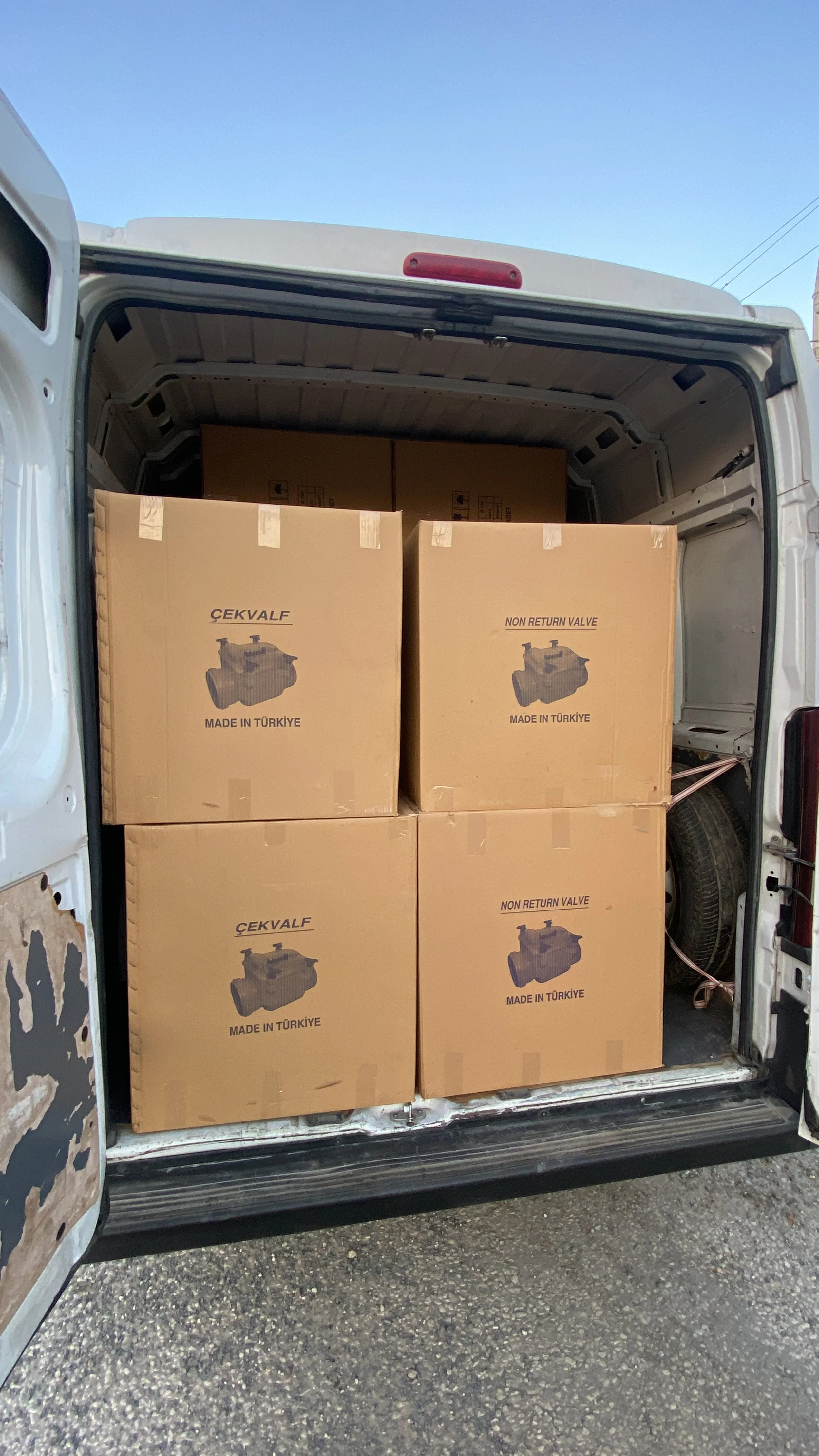The back of a van filled with cardboard boxes labeled 'ÇEKVALF', 'Made in Türkiye', and 'Non Return Valve'.