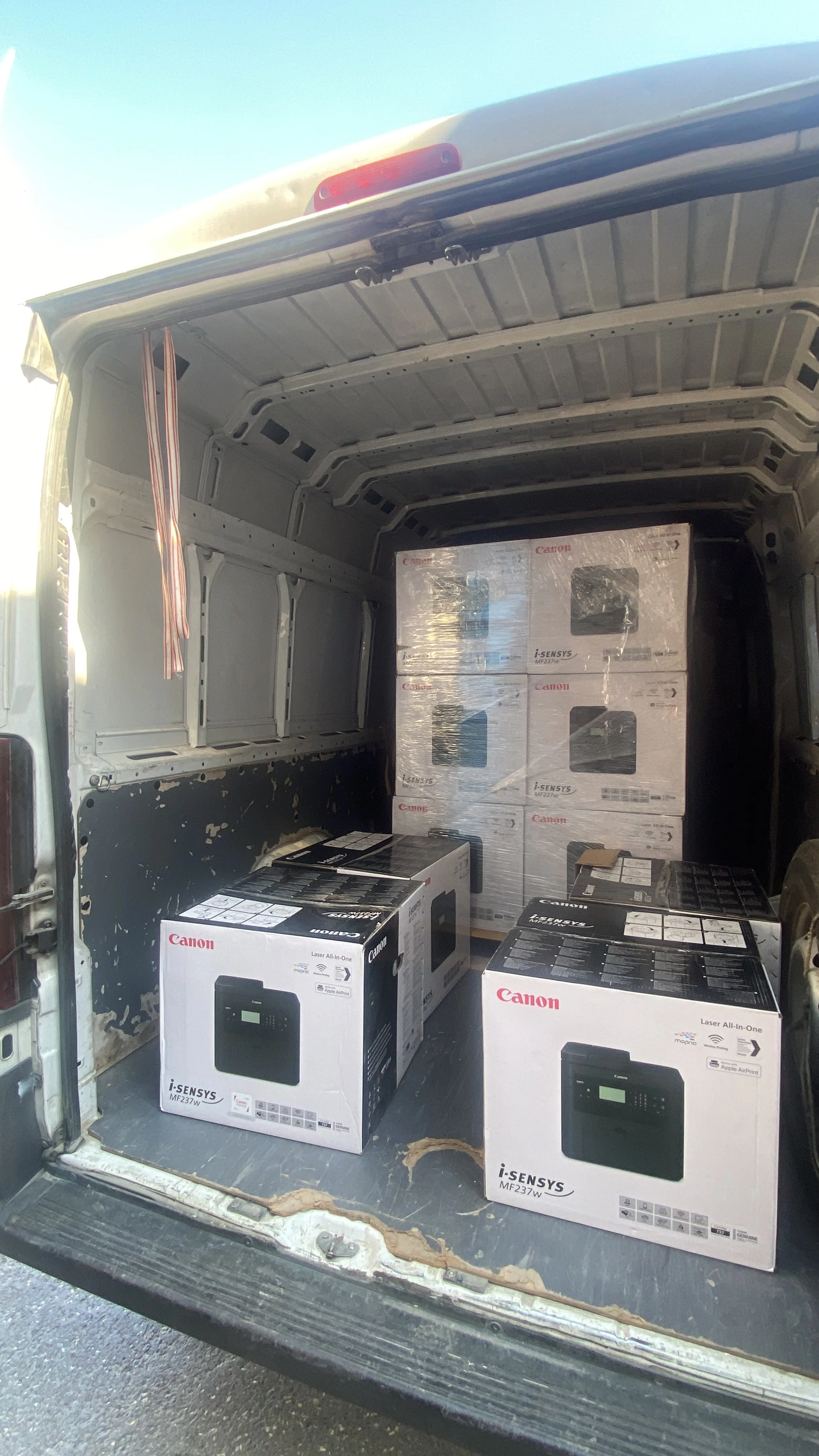 The back of a cargo van with four boxes of Canon printers inside, three on the floor and one stacked upright on a pallet.