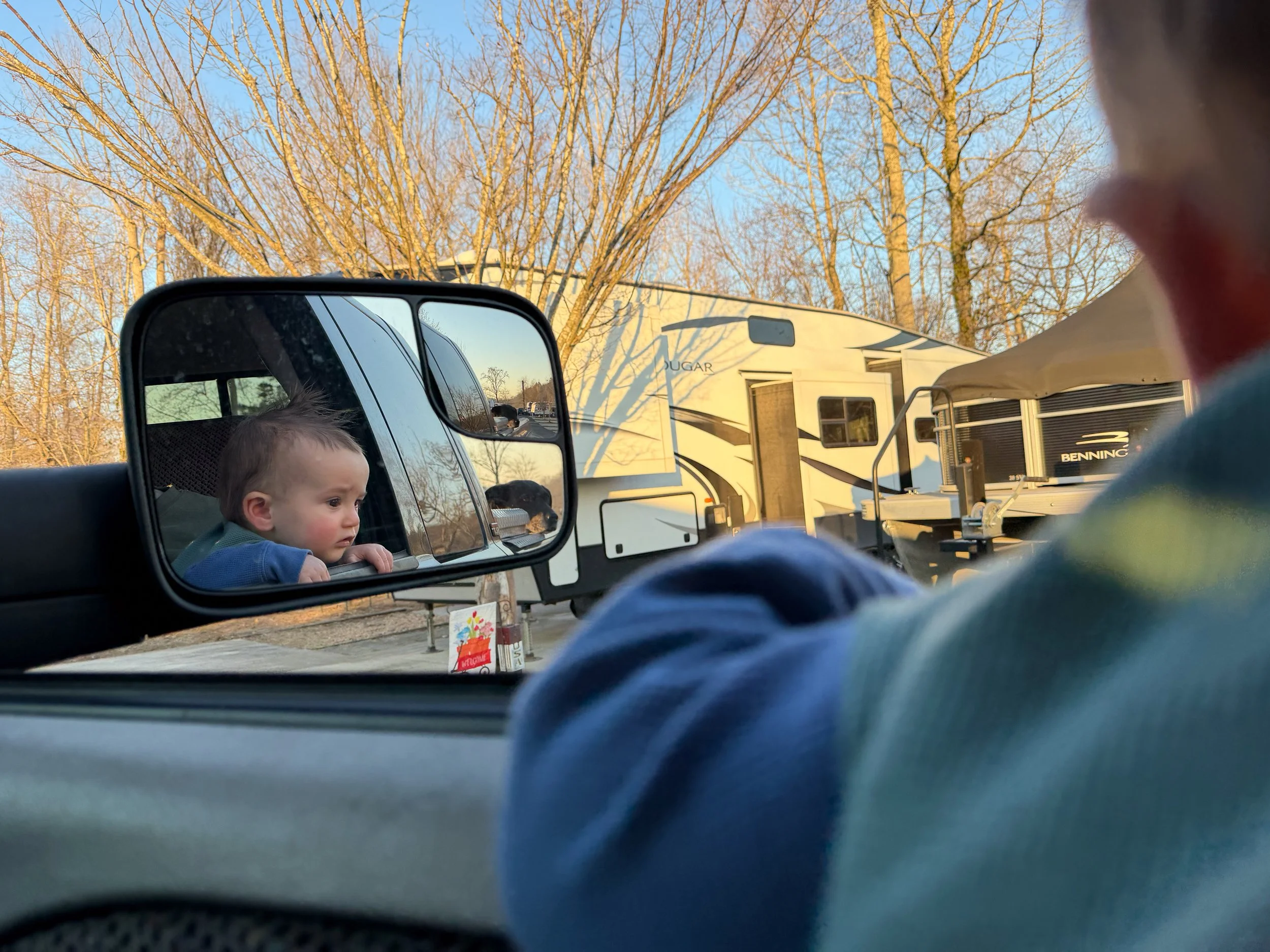 Baby reflected in a truck side mirror while parked at a campground, capturing everyday life raising a baby on the road.