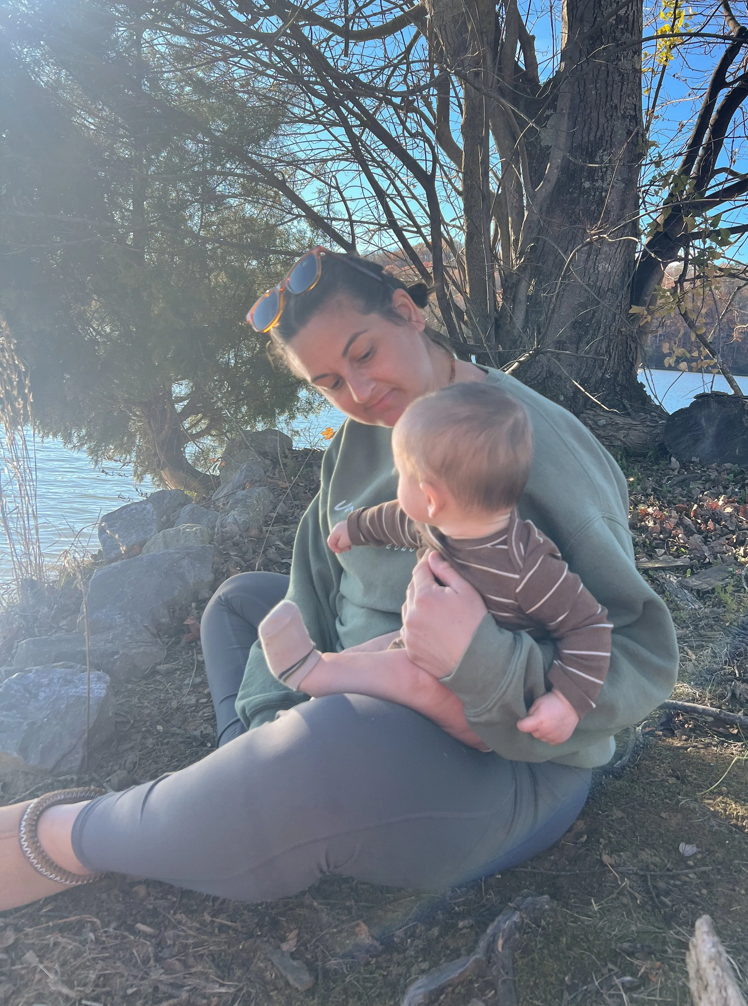 Mother and baby sitting by a lakeside in East Tennessee during late winter, reflecting on slow motherhood and seasonal transition into spring.