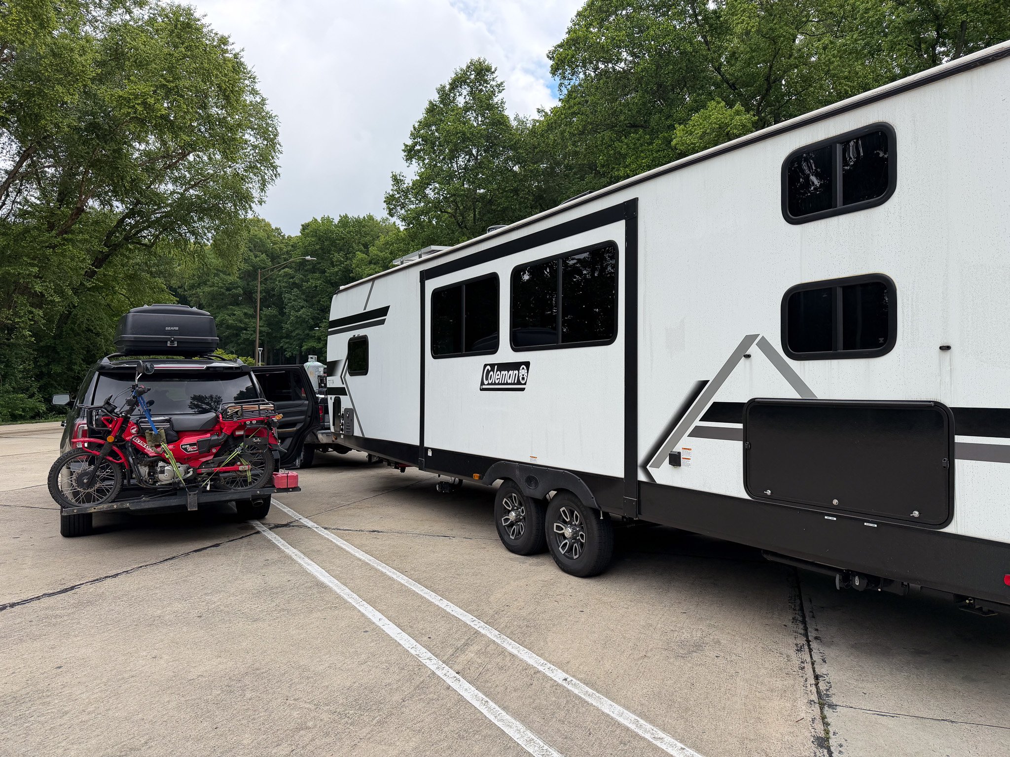 Travel trailer and SUV with a motorcycle parked during a family RV travel day.