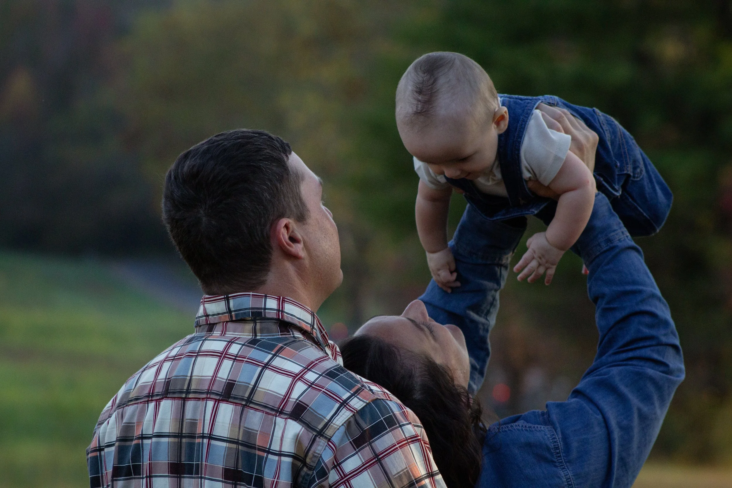 Parents lifting their baby together outdoors, capturing connection and presence in everyday family life