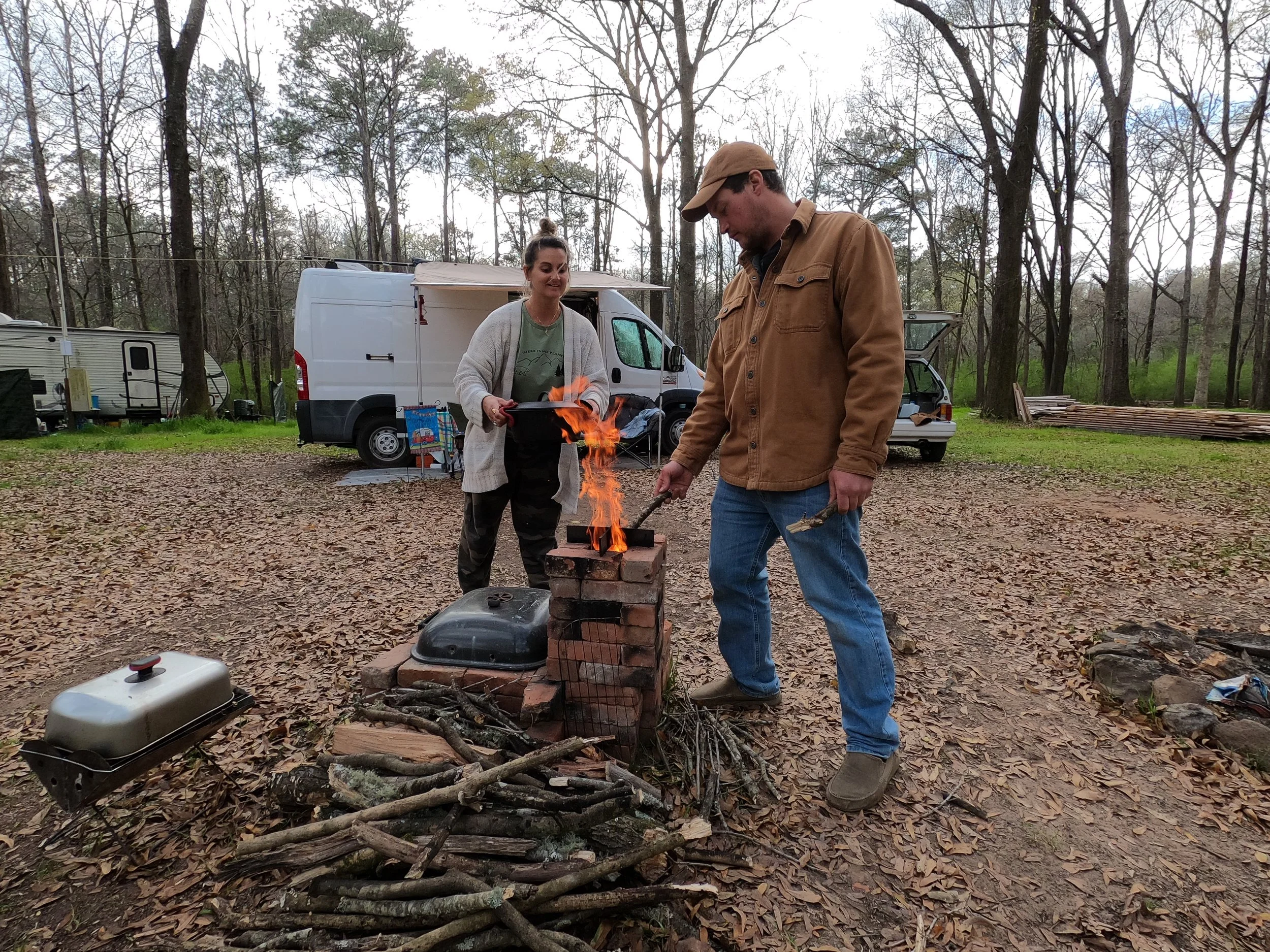Couple cooking over a campfire while living in a white van, representing the evolution of vanlife and long-term nomadic living.