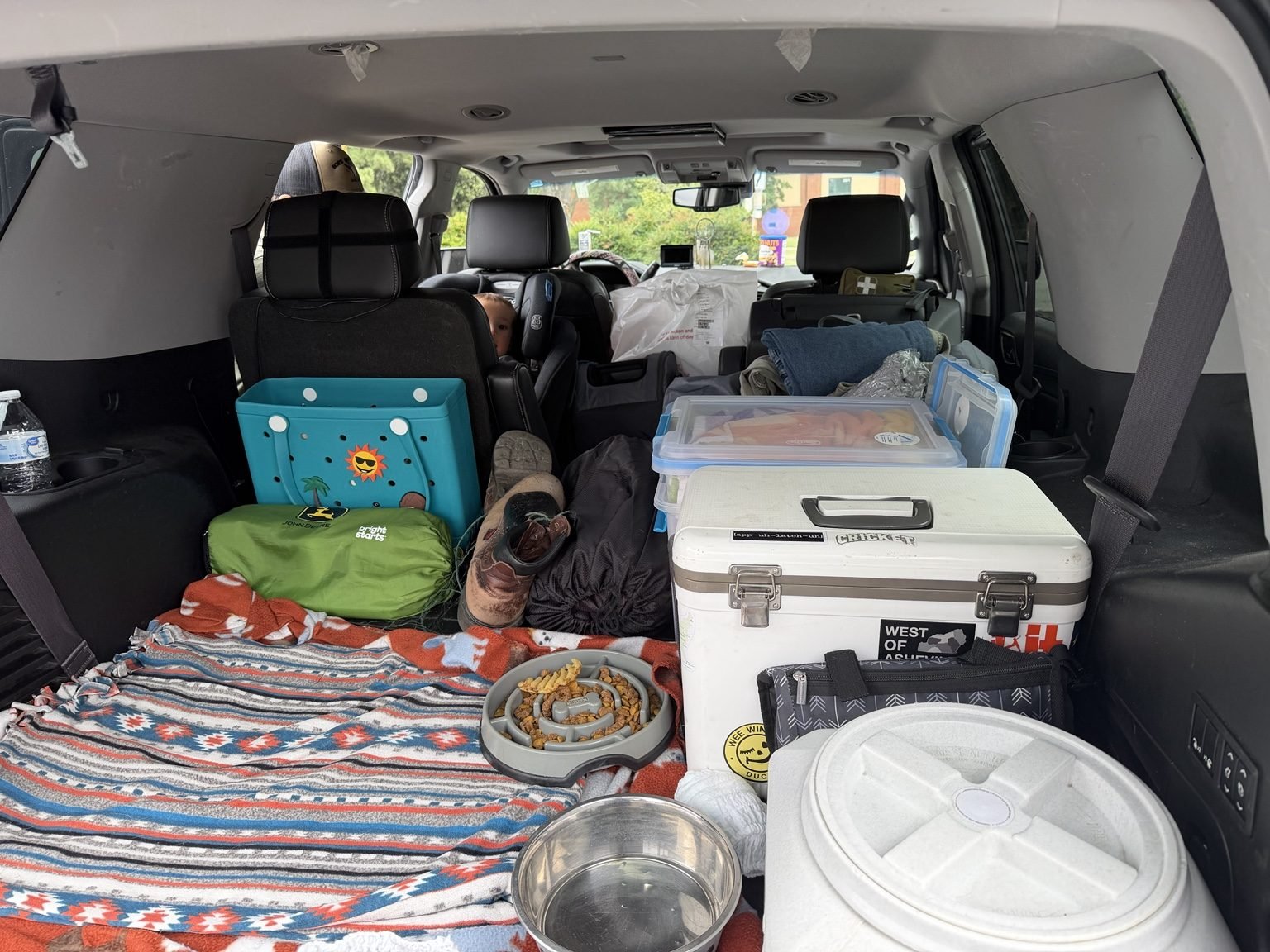 Packed Yukon cargo area organized with a cooler, storage bins, blankets, dog bowls and toddler travel gear.