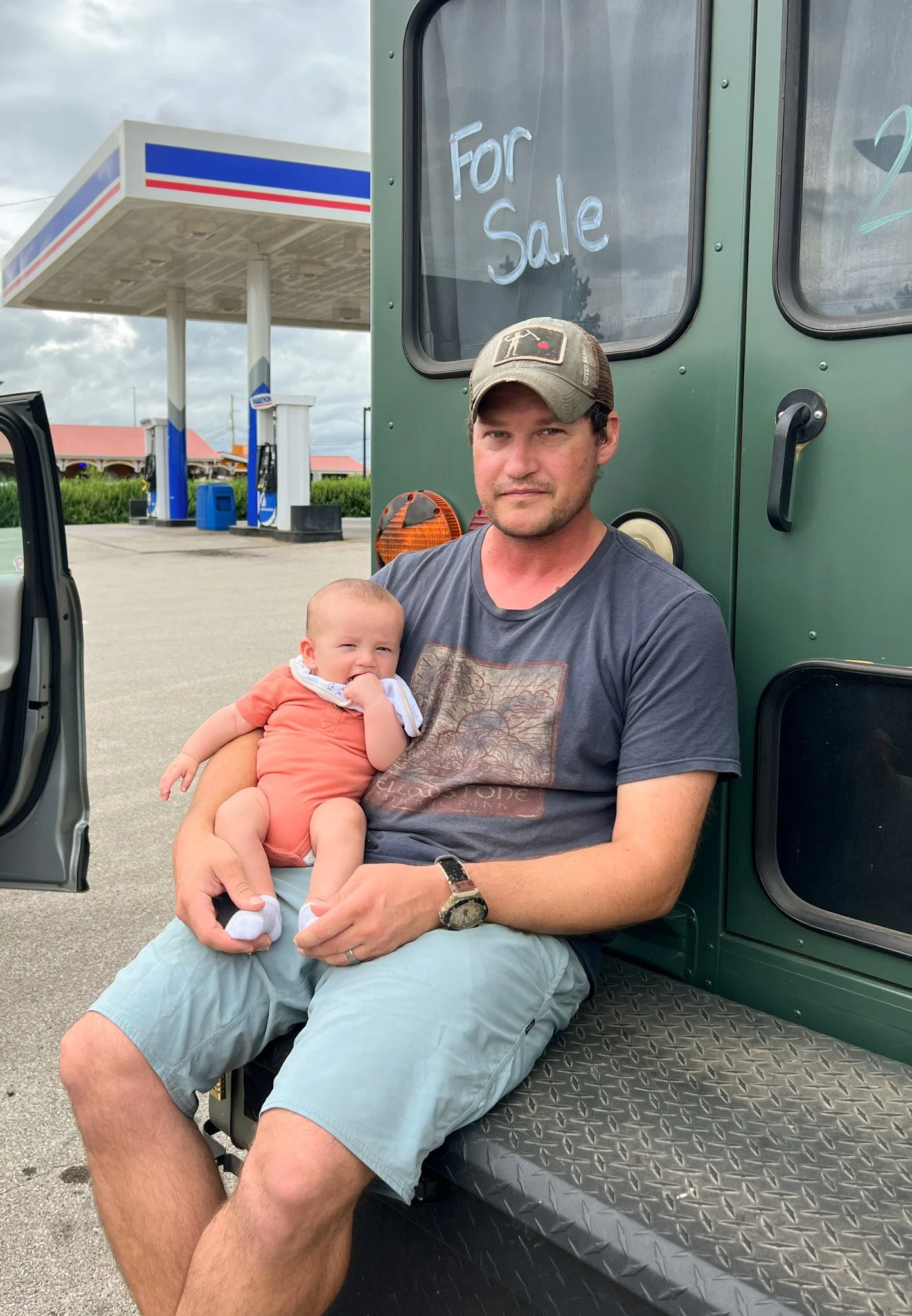 Father holding his baby during a roadside stop while reuniting after time apart, showing stability while raising a baby on the road