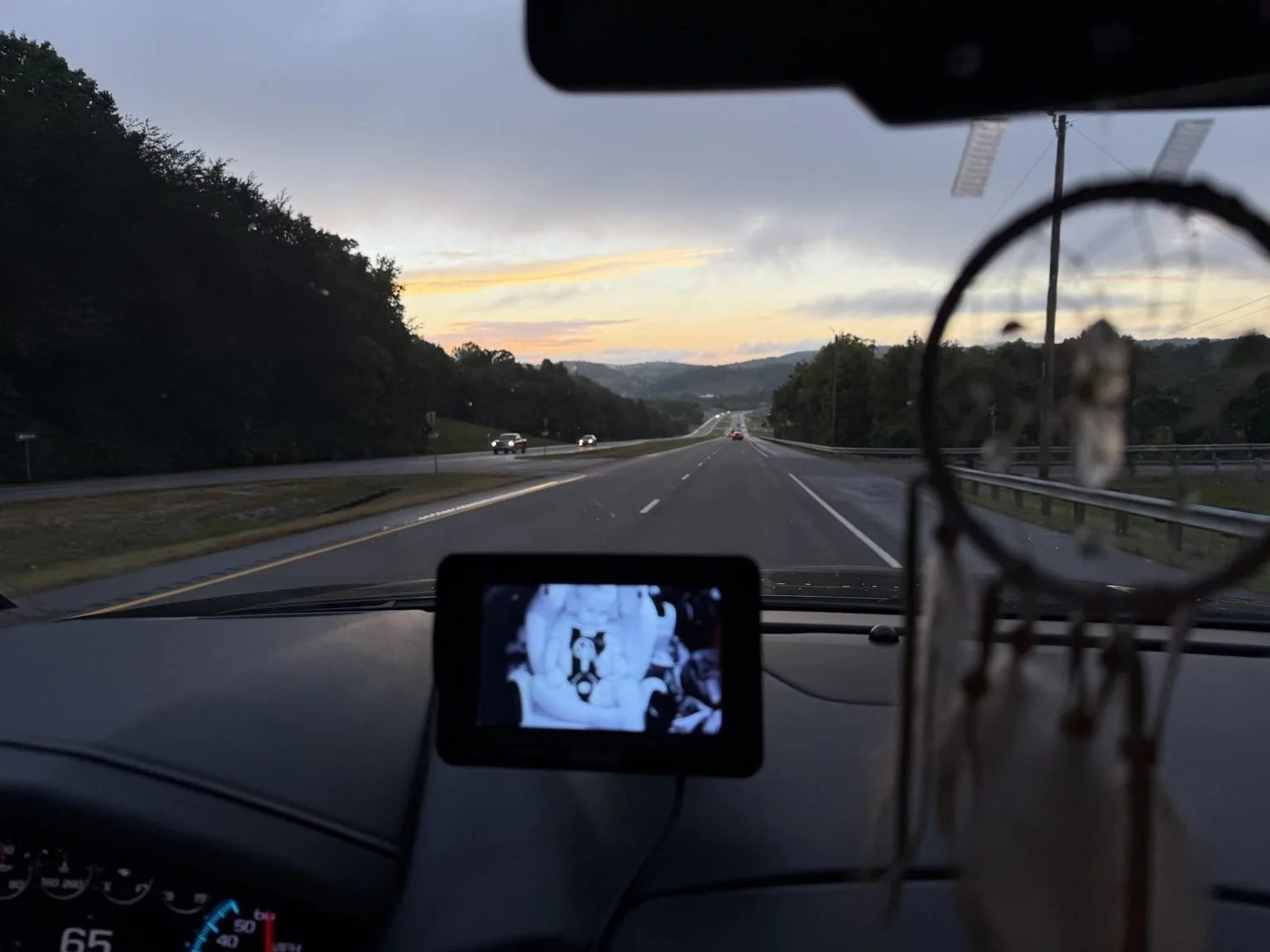 Highway through the mountains at sunset with a toddler car seat monitor visible from inside the family SUV.