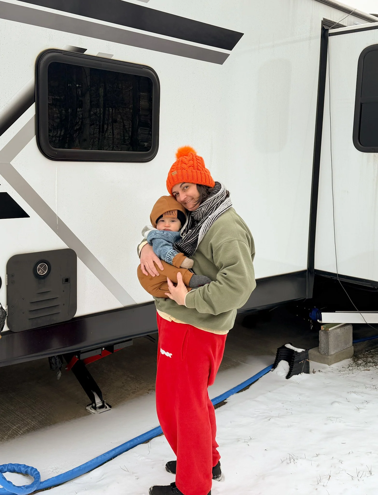 Mother holding her baby outside their RV in winter, capturing everyday life raising a baby on the road
