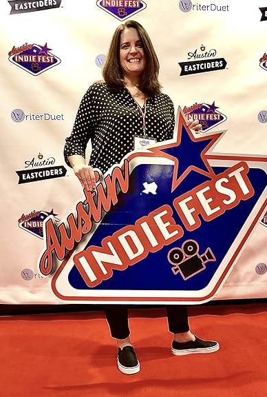 Woman holding an Austin Indie Fest sign at a promotional event with a step-and-repeat backdrop featuring Indie Fest and Eastciders logos.