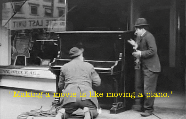 Two men working on a piano in a workshop, with one kneeling and the other standing, while a quote about making movies plays.