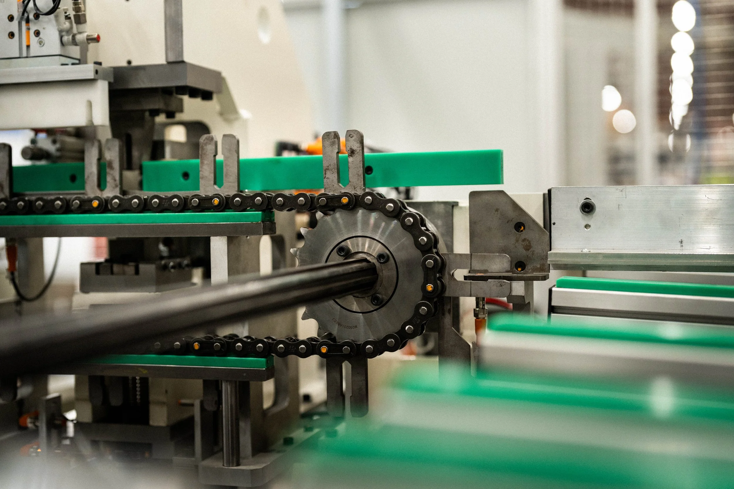 Une machine industrielle avec une chaîne et une roue dentée, probablement dans une usine ou un atelier de fabrication.