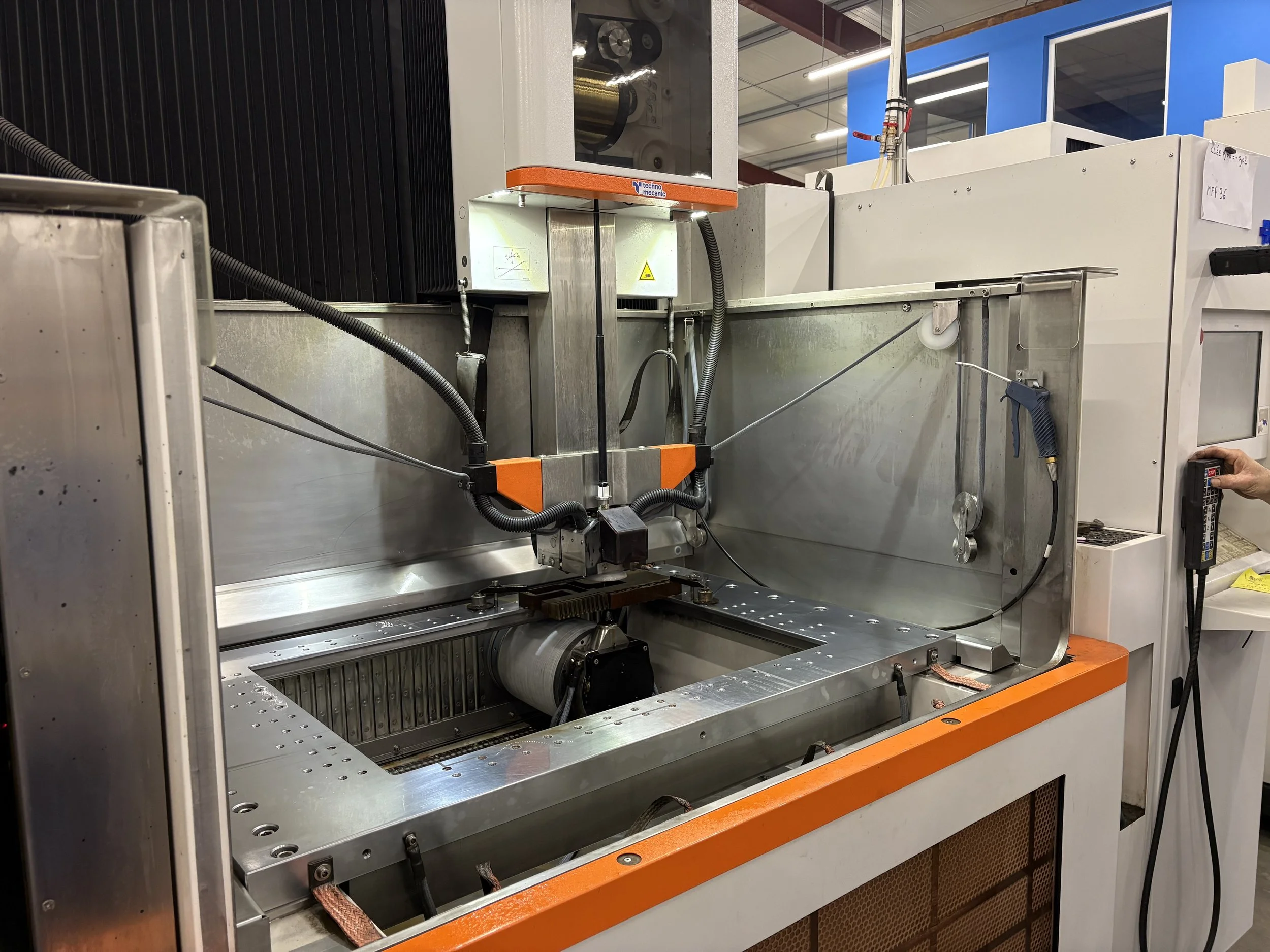 Une machine de fabrication industrielle avec un bras robotisé, une cabine de protection et un panneau de contrôle, située dans une usine.