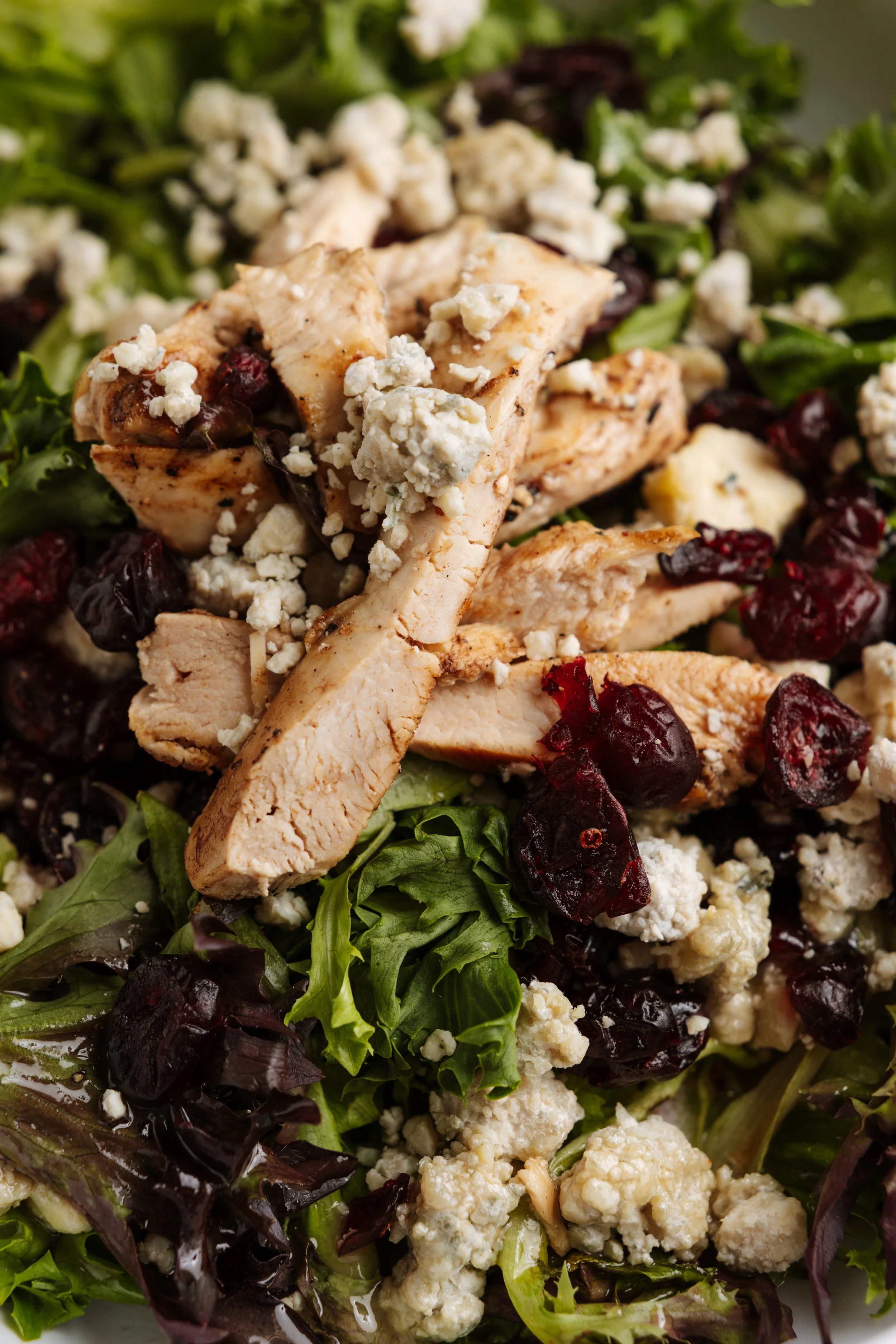 Fresh mixed greens salad topped with grilled chicken, blue cheese crumbles, dried cranberries, and possibly walnuts.
