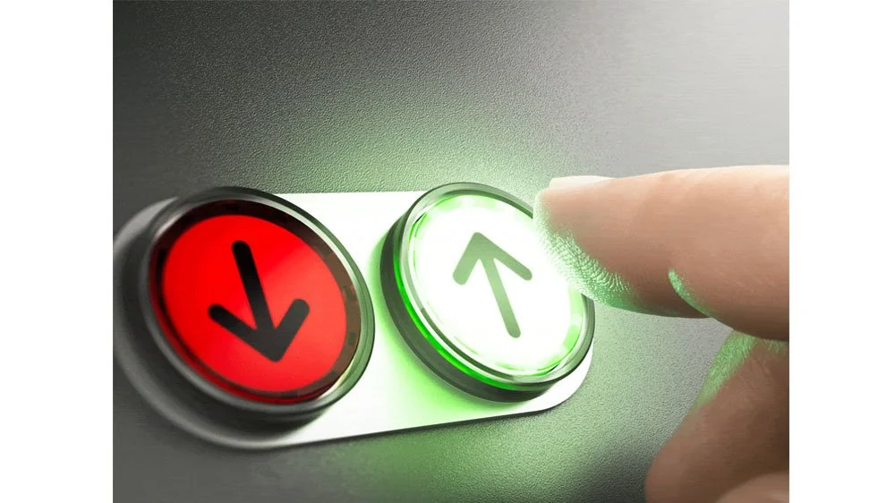 Person pressing the green upward arrow button, with red downward arrow button next to it, on an elevator control panel.