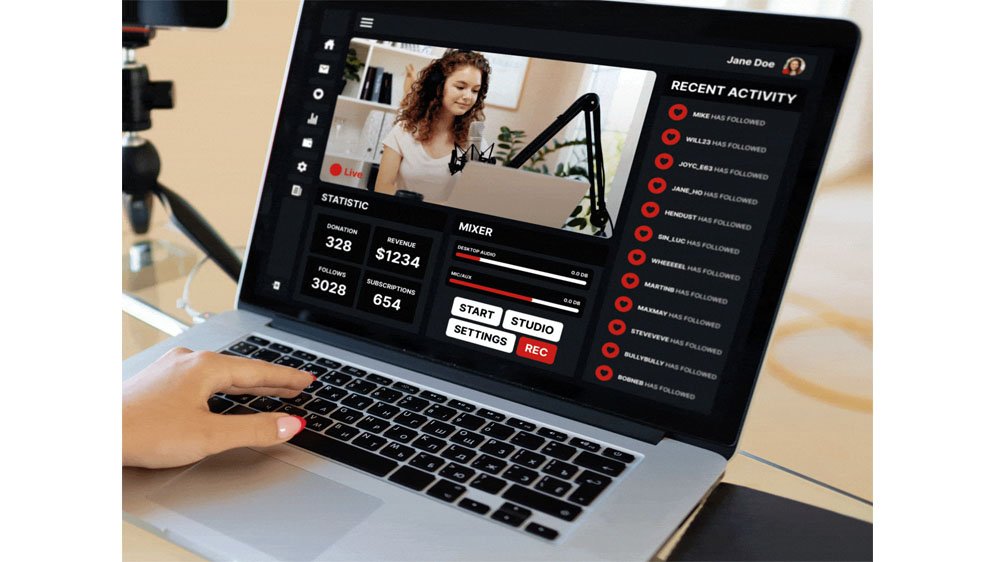 A person uses a MacBook laptop to stream a live video of a woman recording in a studio, with statistics, mixer controls, and recent activity on the screen, and a camera on a tripod nearby.