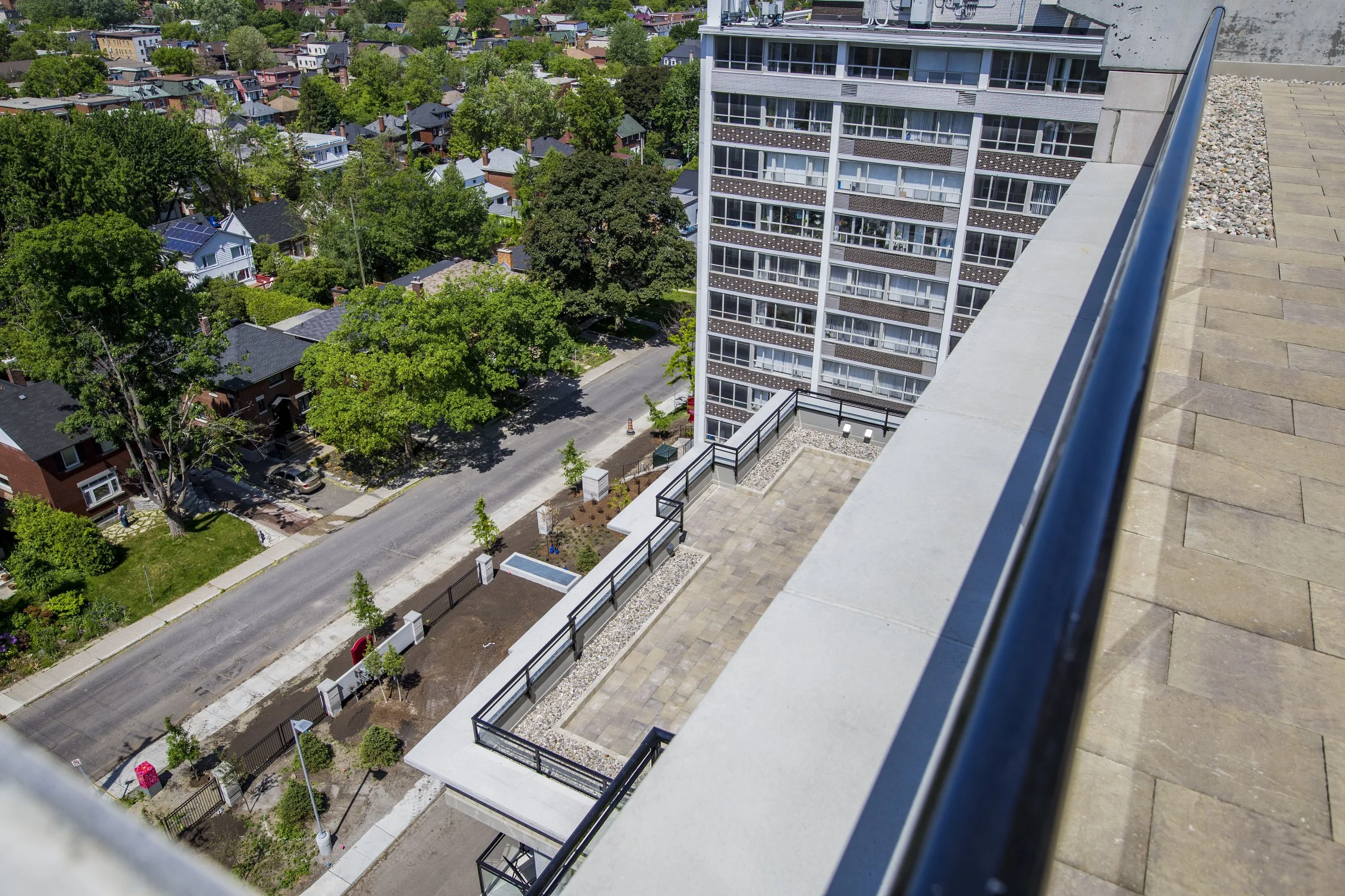 View from a high-rise balcony showing a city street with trees, residential houses, and a tall apartment building.