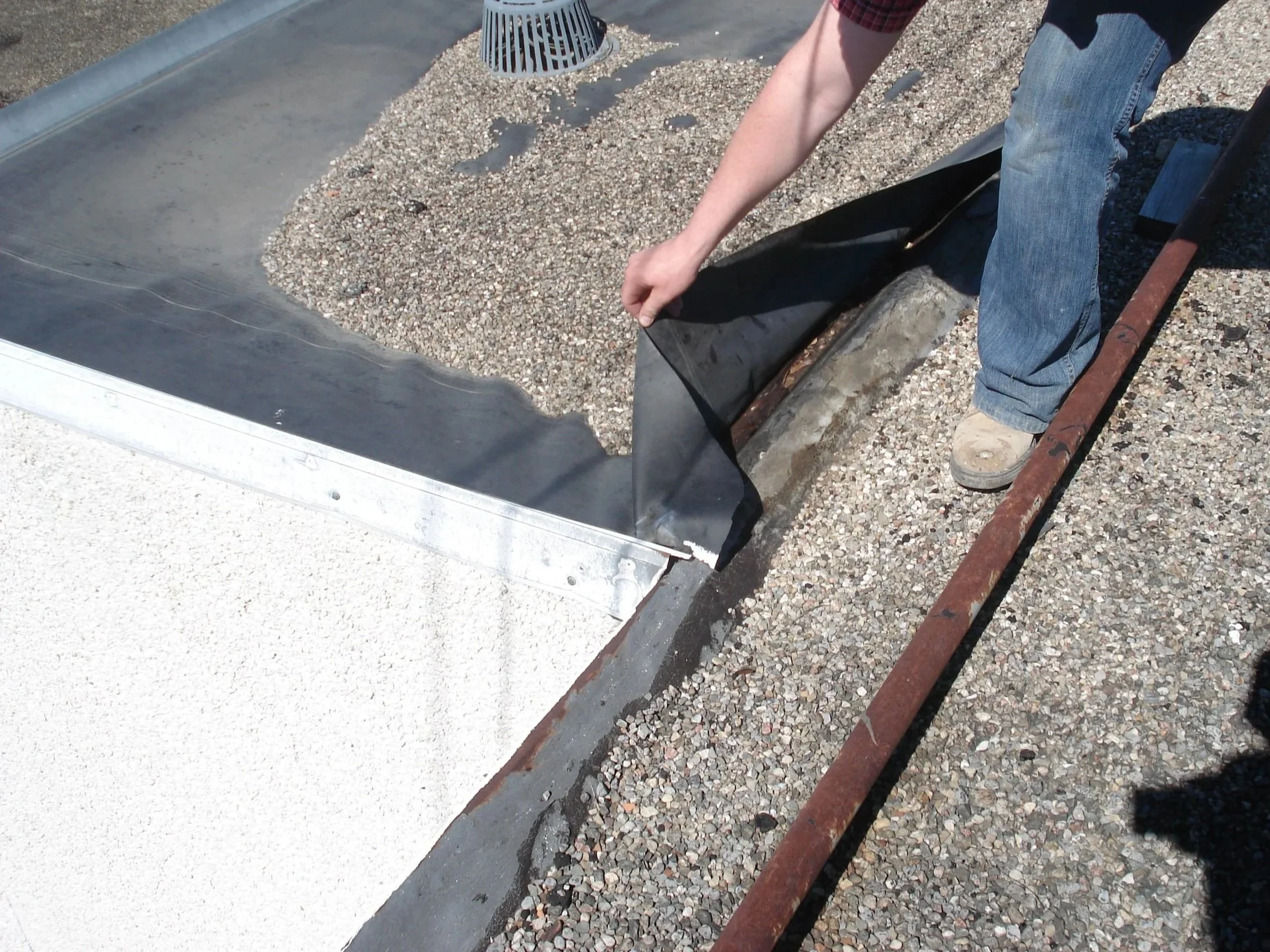 Worker installing roofing gravel on a rooftop, using a metal rake.