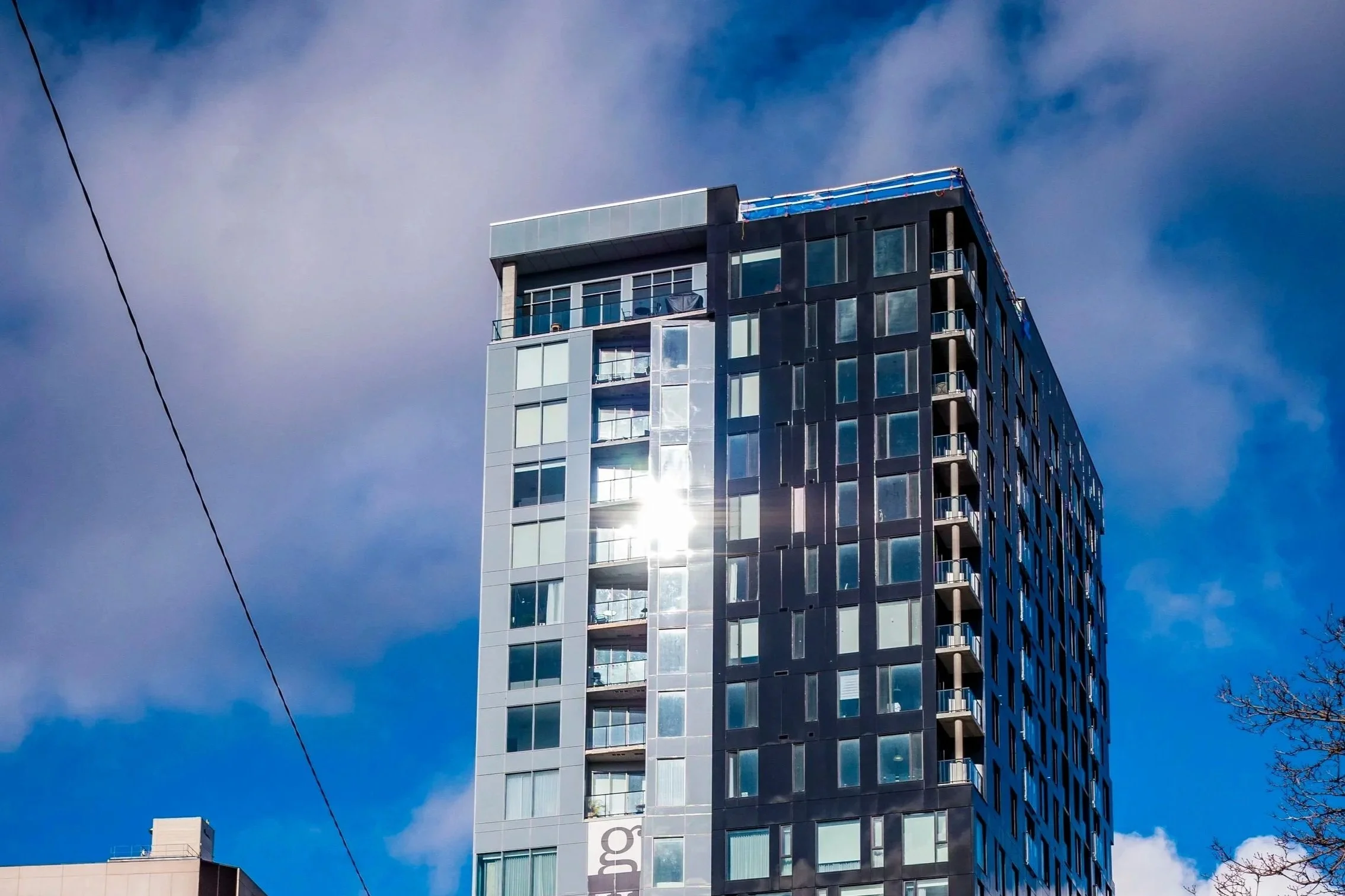 A modern high-rise building with glass balconies and black and white exterior panels, set against a blue sky with some clouds.