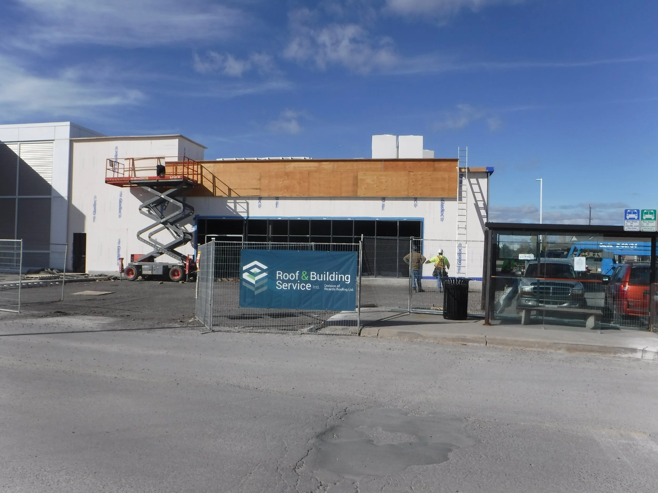 Construction site with building under renovation, workers, scaffolding, and construction signs, with a blue sky in the background.
