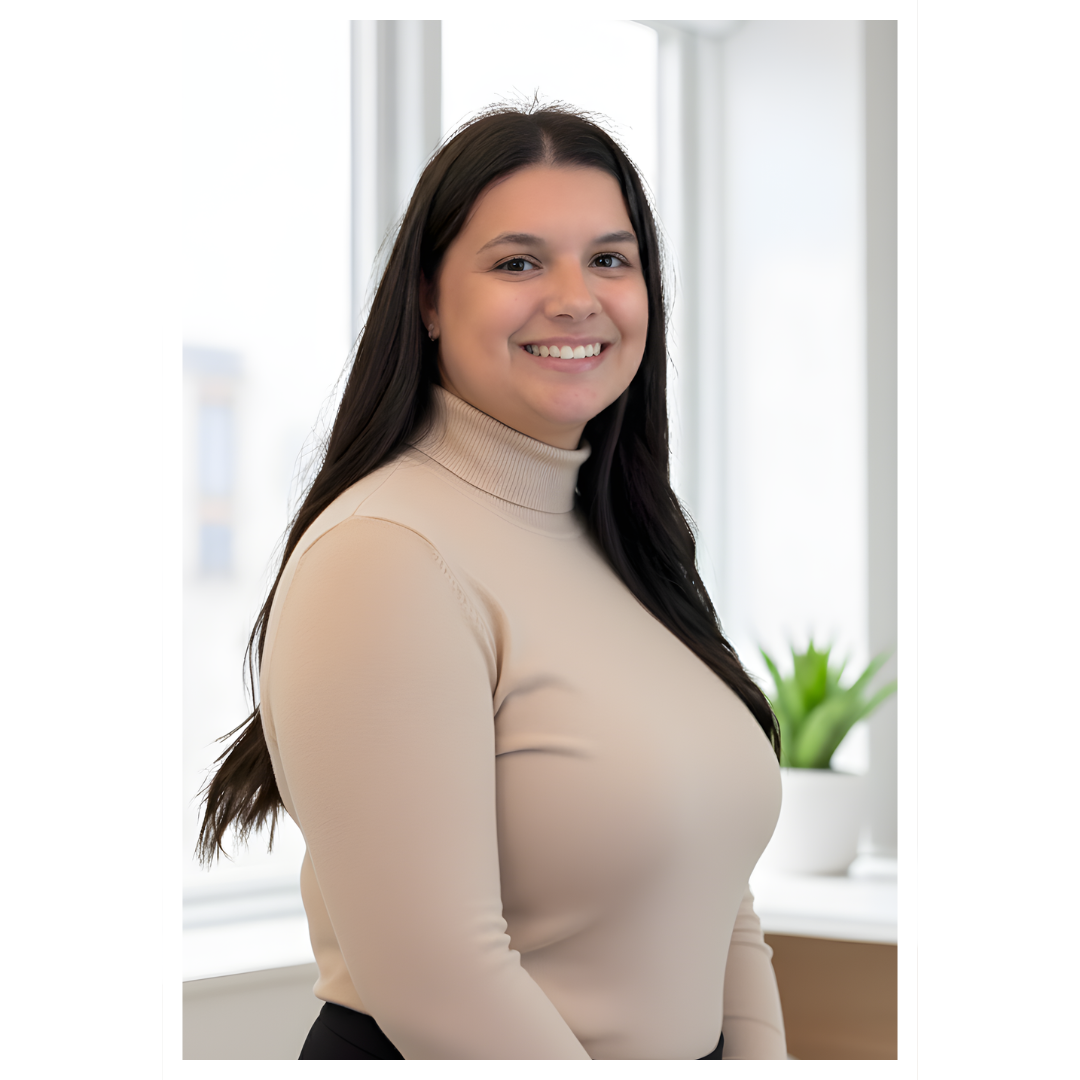 Jeune femme souriante en intérieur, portant un haut beige à col roulé, avec une plante verte en arrière-plan.