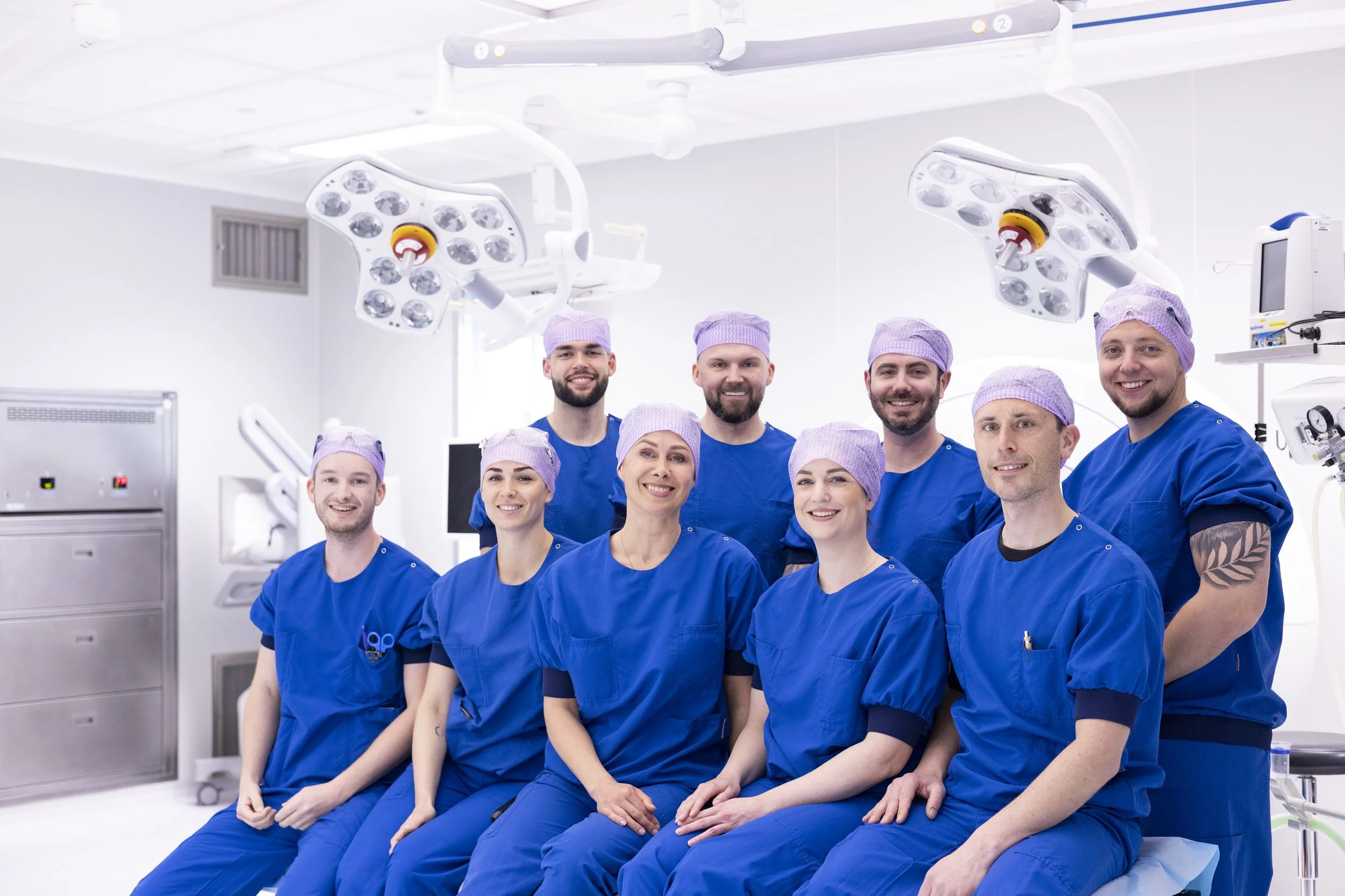 Tien medisch personeel in blauw uniform en paarse petten in operatiekamer.