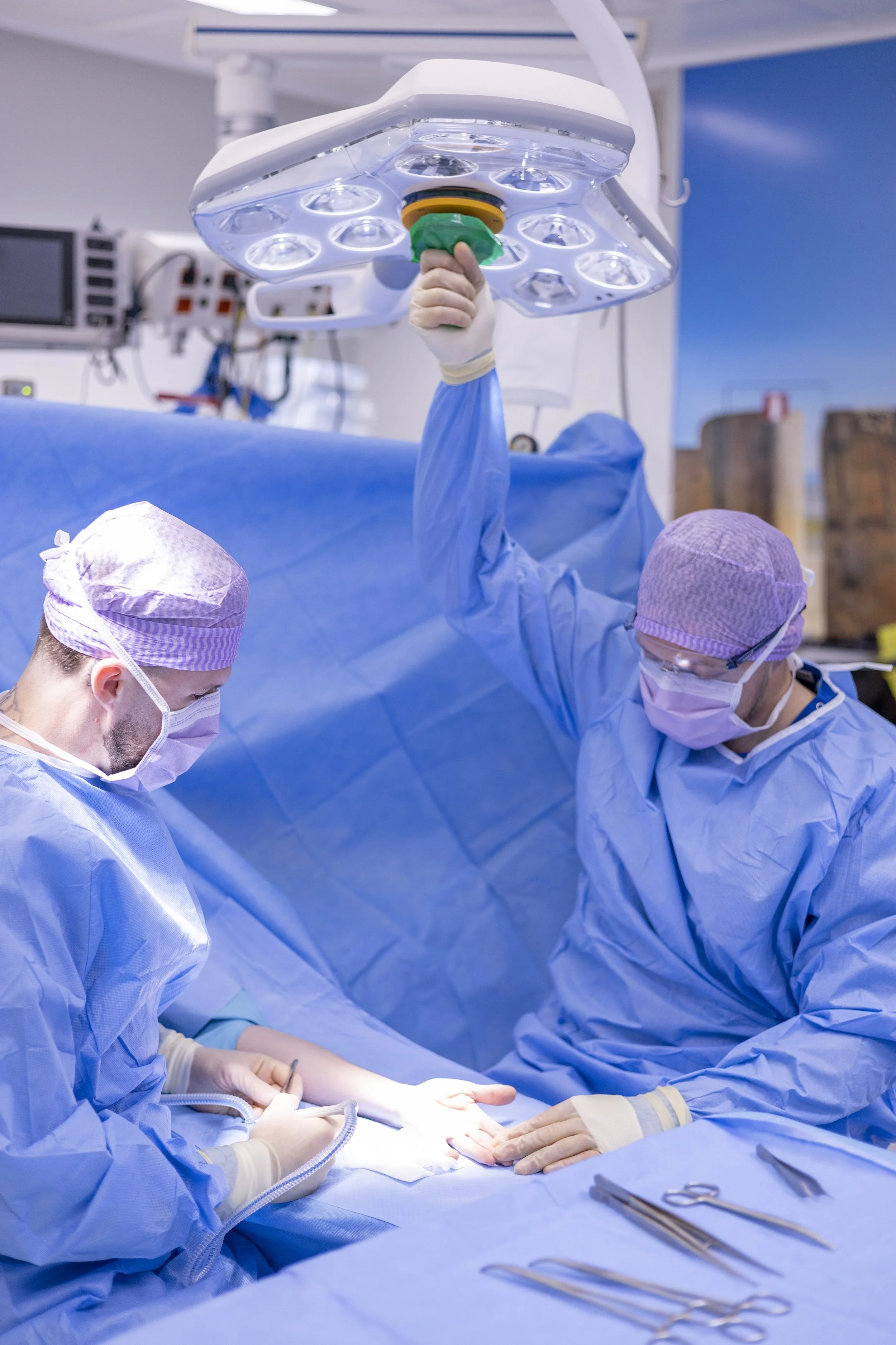 Fotografie van een team chirurgen die een operatie uitvoeren in een operatiekamer, met medische instrumenten op tafel en een plafondlamp erboven.