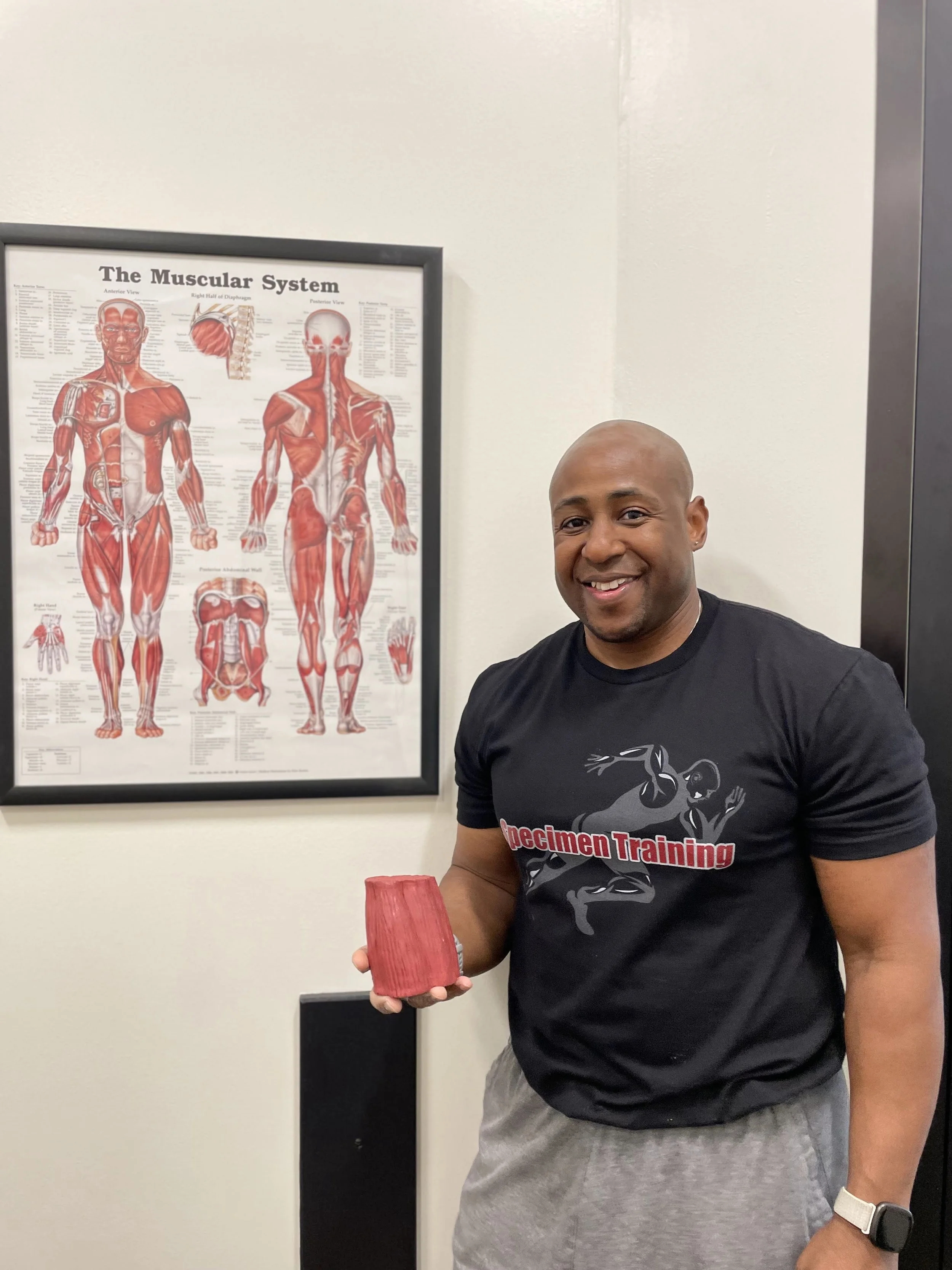 Coach Eric Evans holding a one-pound model of muscle beside a muscular system chart