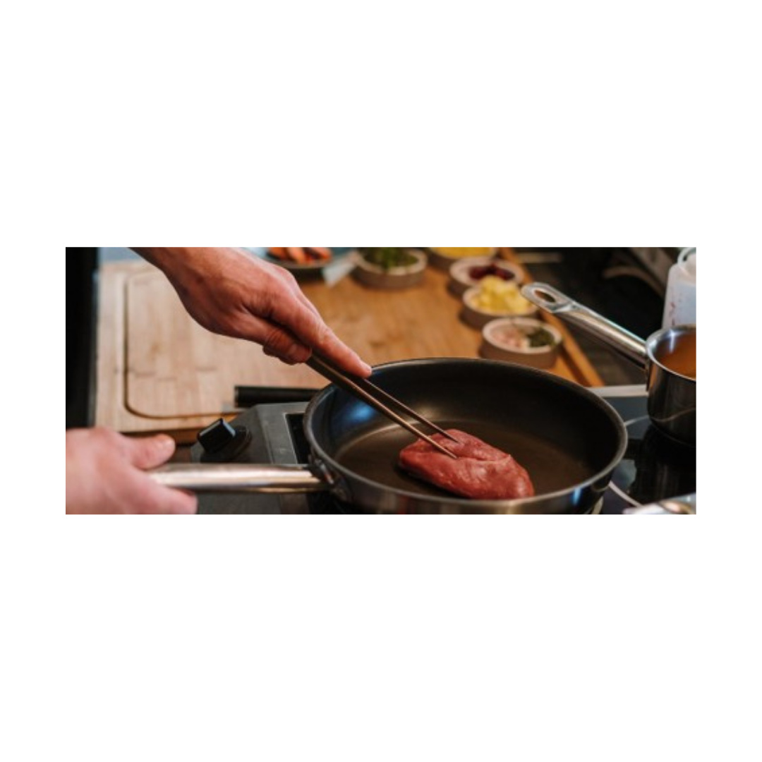 Hand using tongs to sear a steak in a pan as part of a high protein meal prep routine