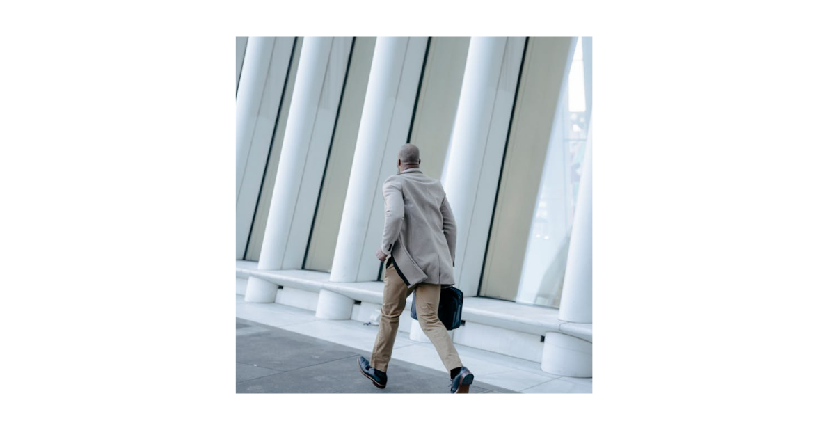A high-achieving professional in a tailored coat strides through a modern office building, briefcase in hand, always moving but never making time for fitness.