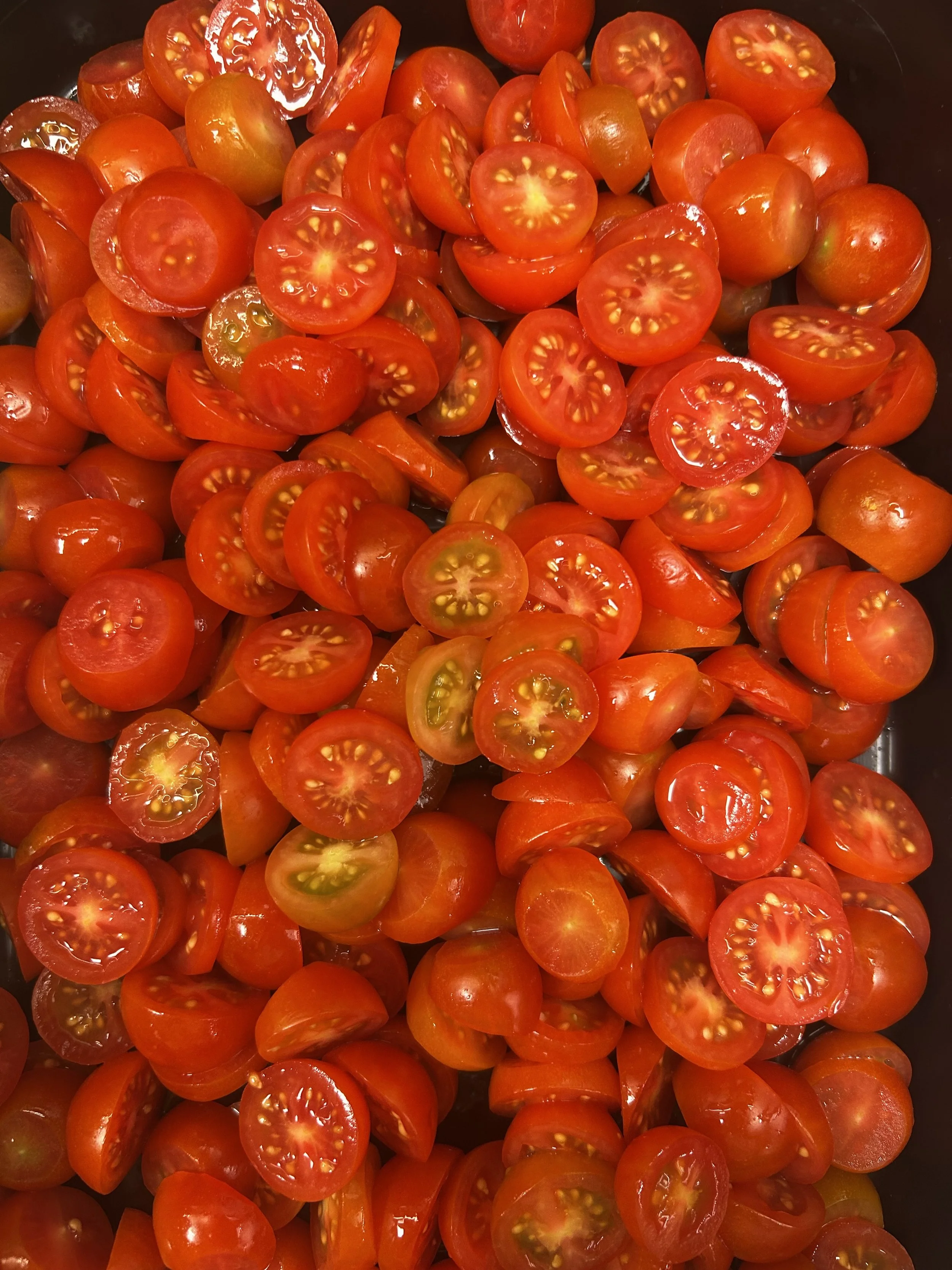A close-up view of numerous halved cherry tomatoes, with red and yellow-orange colors, showing their juicy interior and seeds.