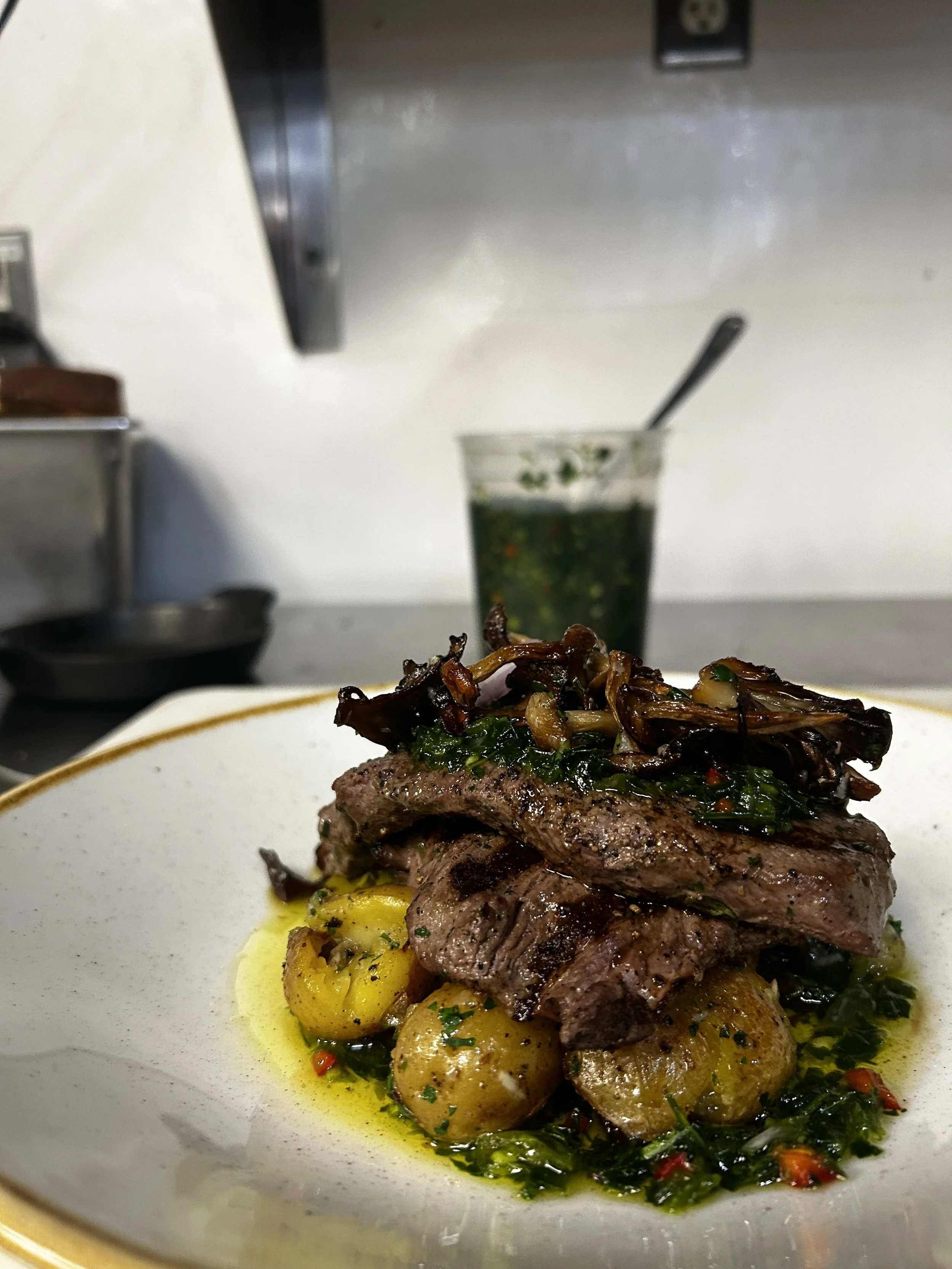 A plate with grilled steak, small roasted potatoes, and sautéed mushrooms with herbs, garnished with chopped herbs and red pepper flakes.