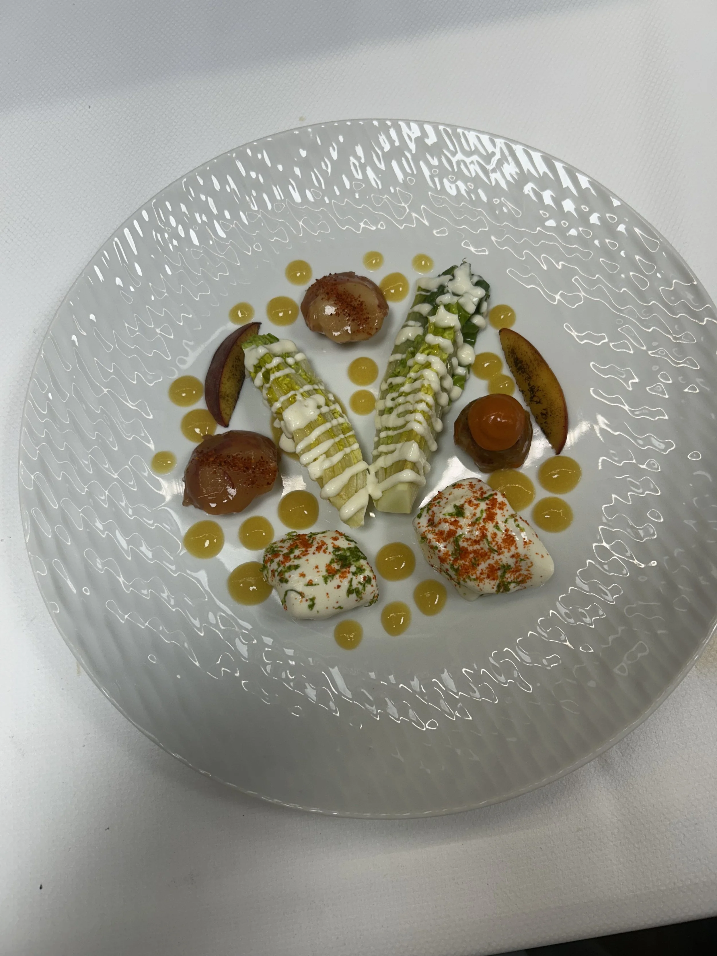 A gourmet plate with two stuffed endives, garnished with sauces, small peaches, and two dollops of creamy white spread topped with herbs and chili flakes.