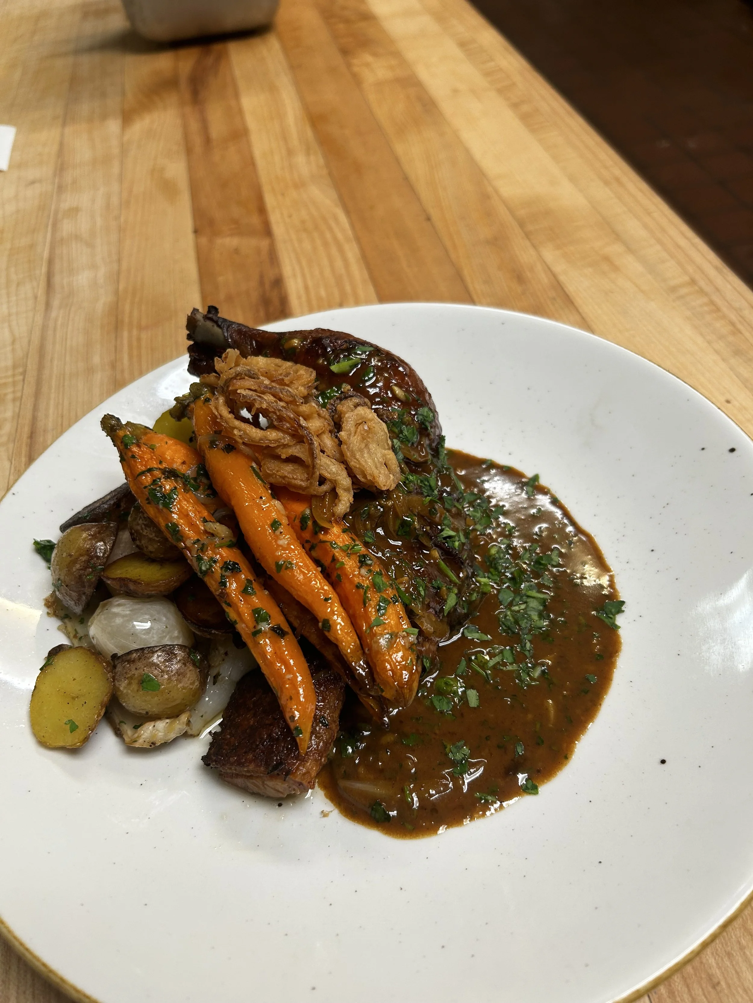 Plate of roasted vegetables including carrots, parsnips, and potatoes with a piece of meat topped with gravy and fried onions, garnished with chopped herbs.