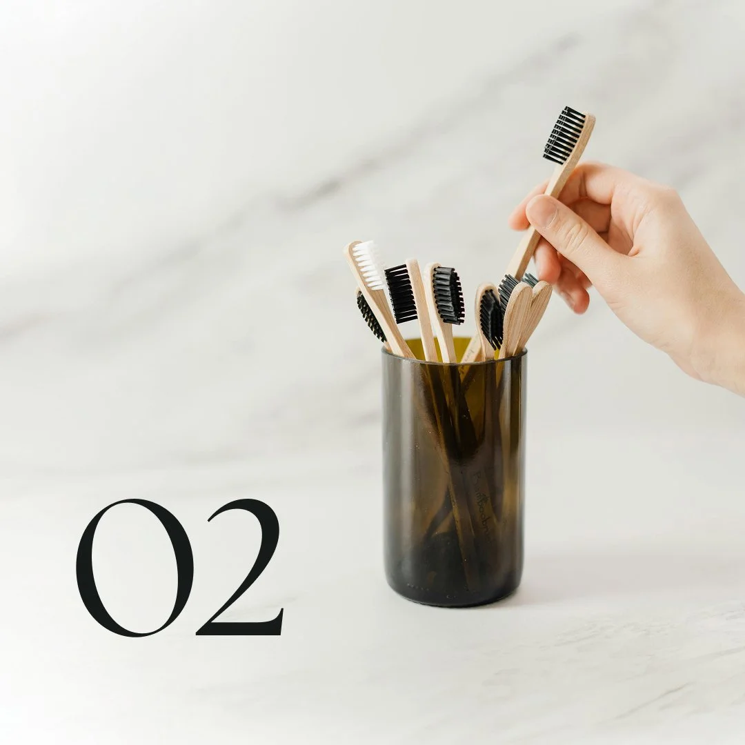 Image of someone taking a wooden toothbrush out of a cup on a marble countertop. 