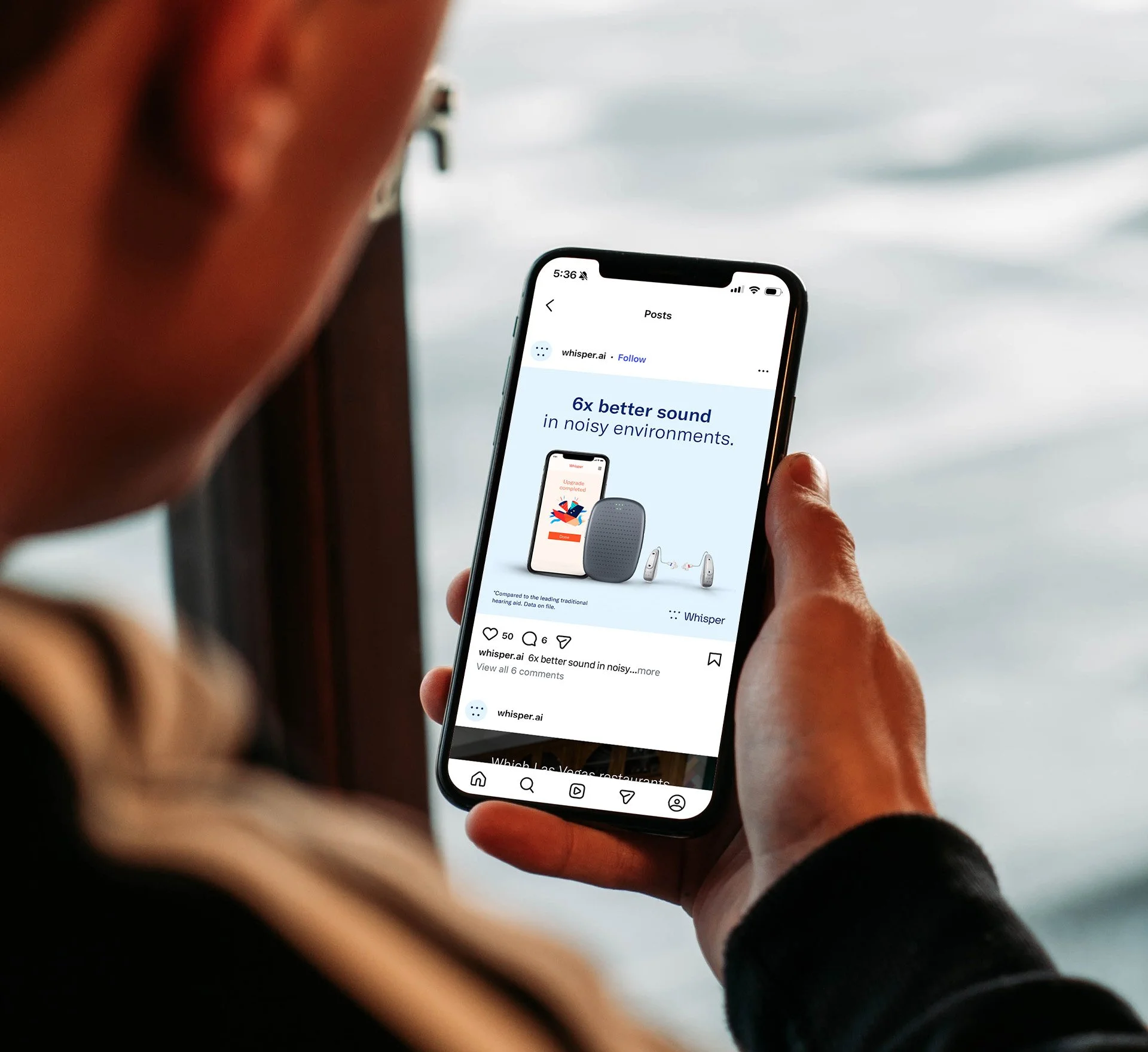 Man holding a cell phone, which shows a social media post promoting a hearing aid.