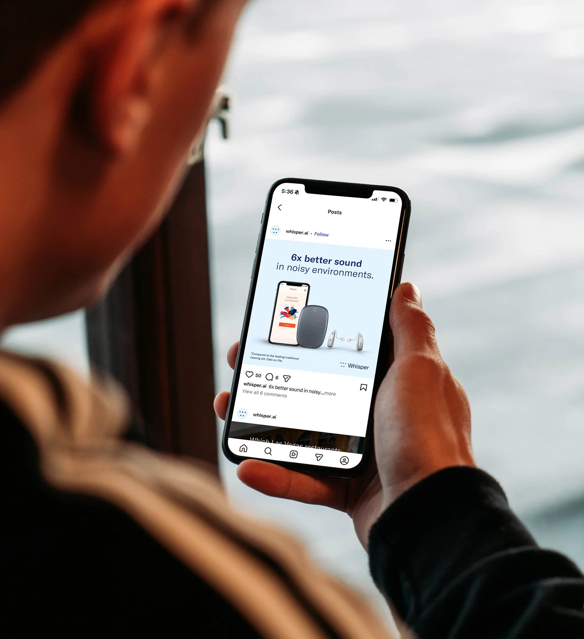 Man holding a cell phone, which shows a social media post promoting a hearing aid.